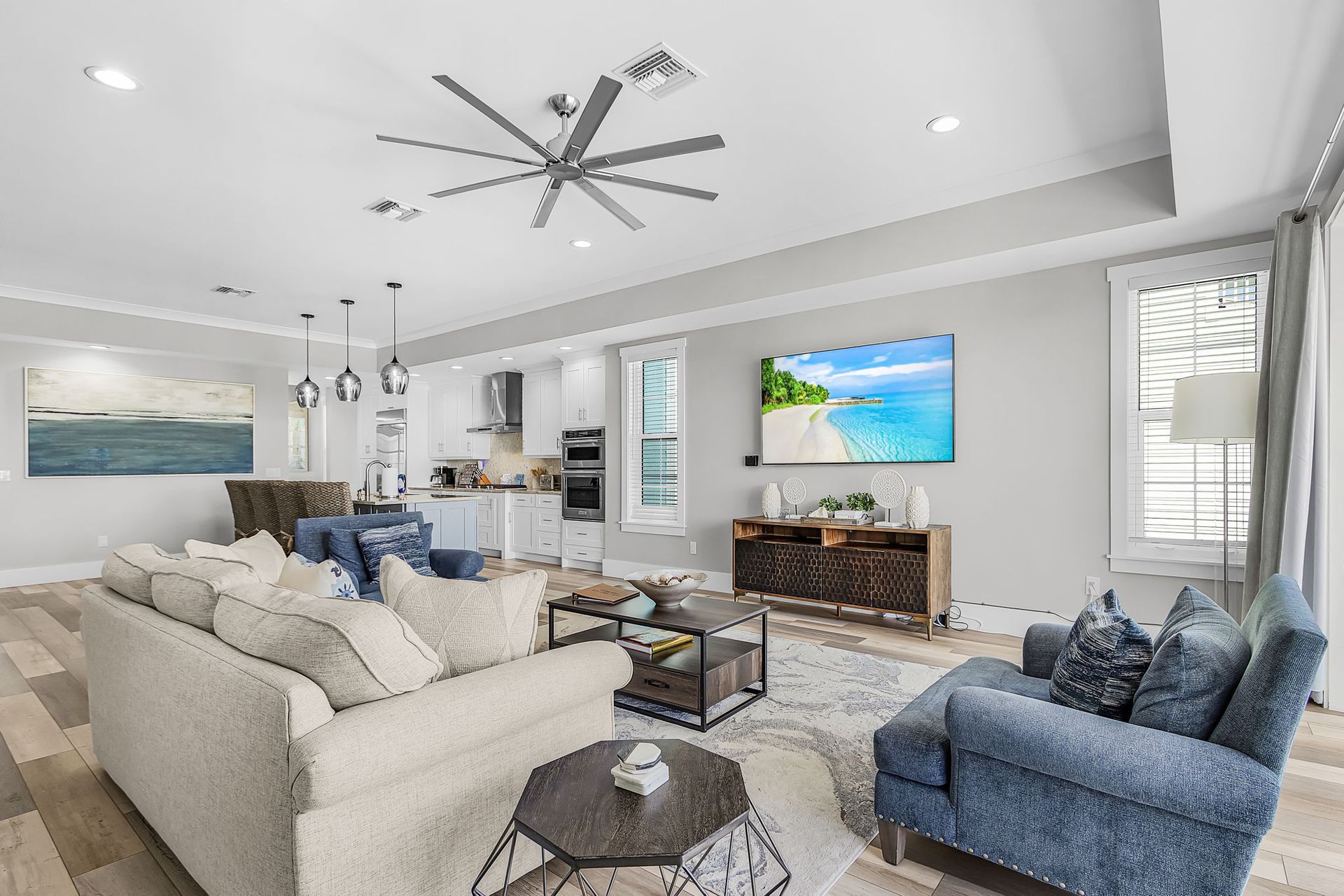 Bright modern living room with cream sofa, blue chairs, wall-mounted TV, and large ceiling fan