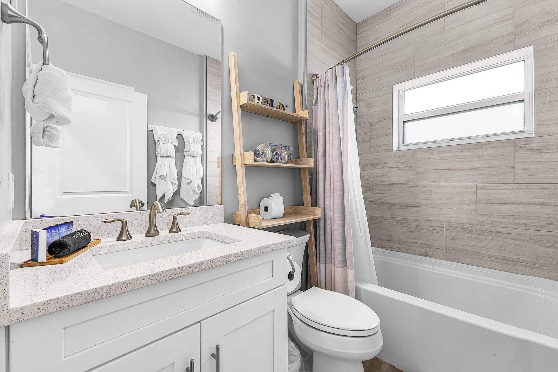 Bright bathroom with vanity, mirror, toilet, bathtub, and wall shelves in white and gray.