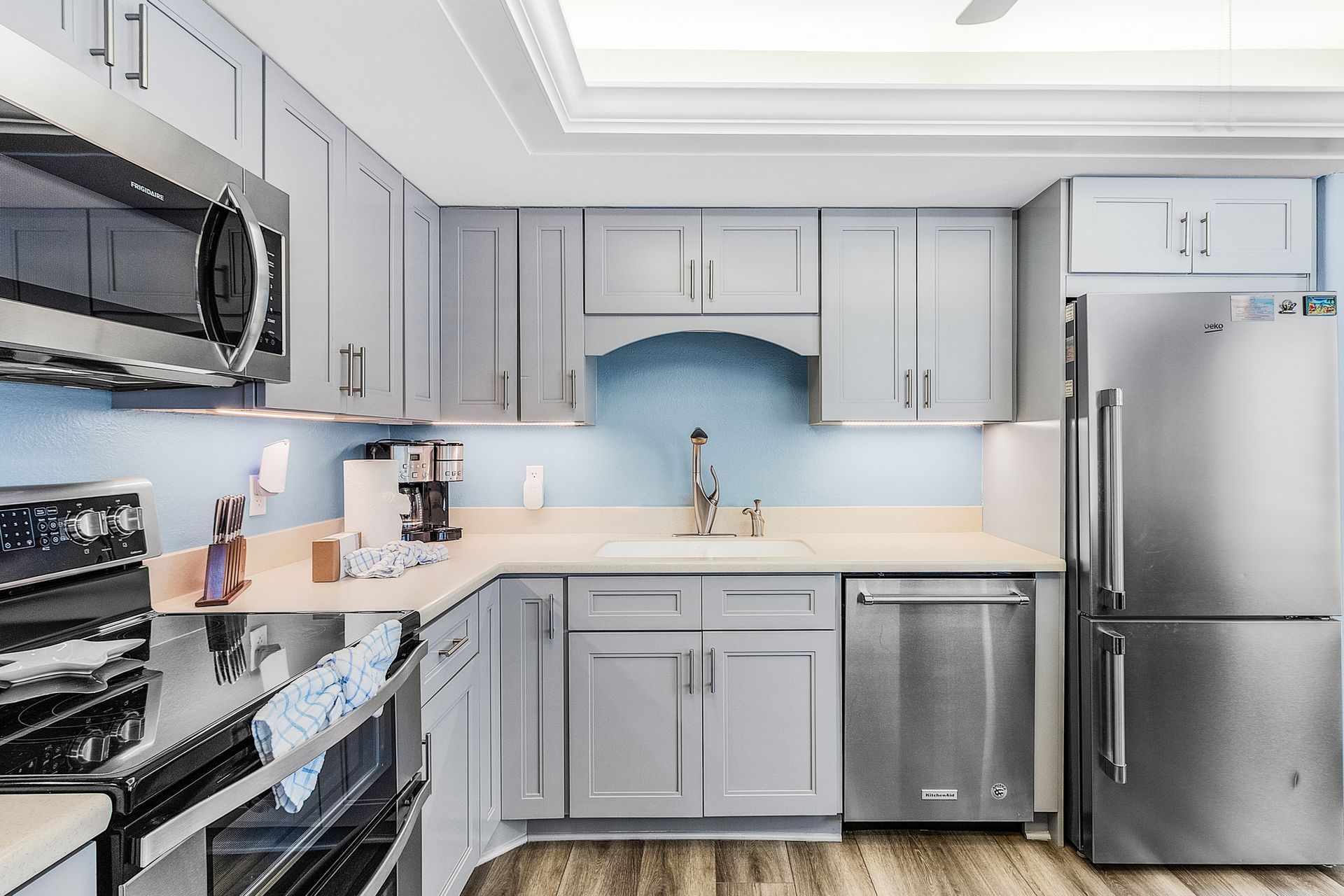 Modern gray kitchen with stainless steel appliances, white countertops, and light wood flooring