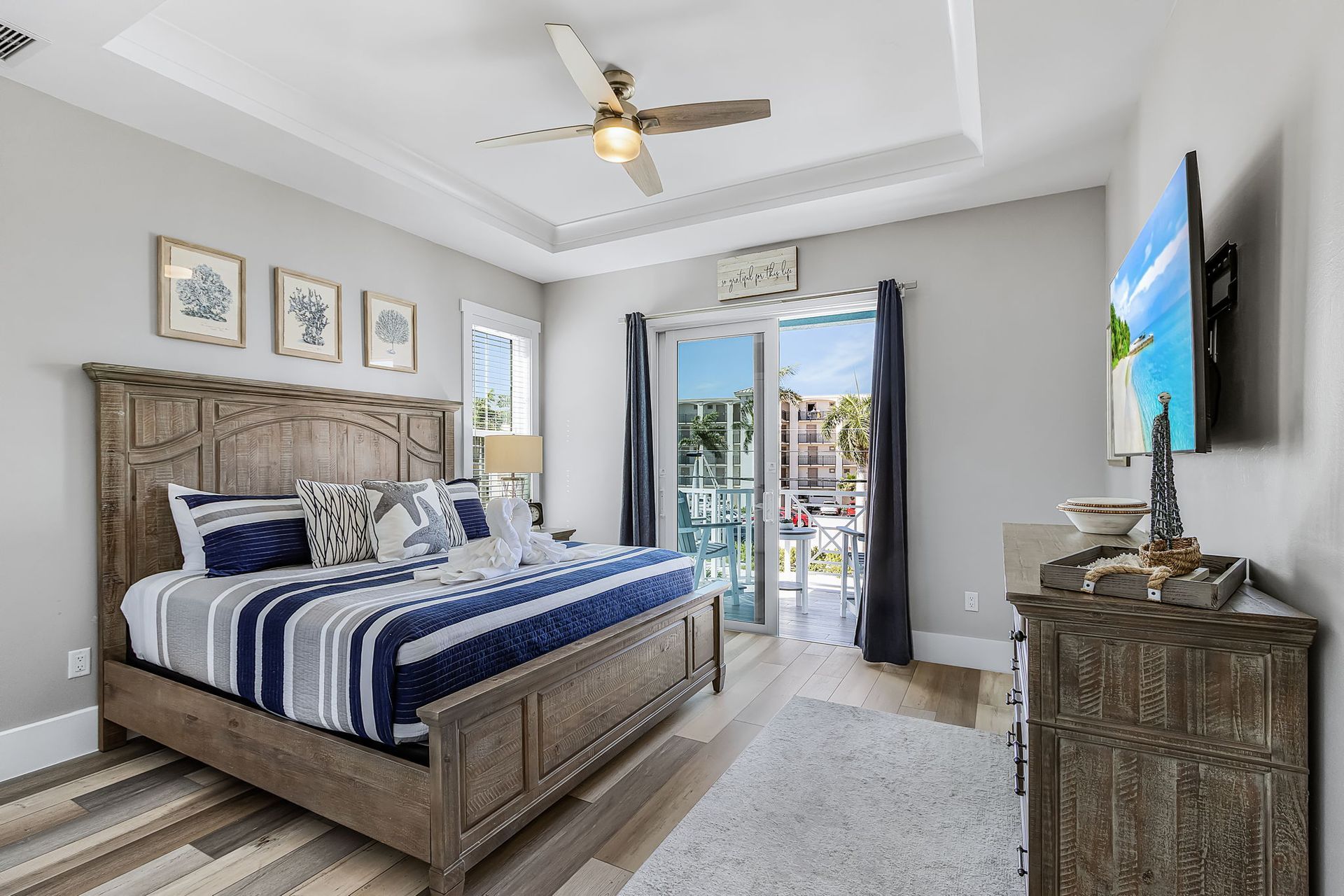 Spacious bedroom with a king bed, blue accents, ceiling fan, dresser, and balcony doors with city view