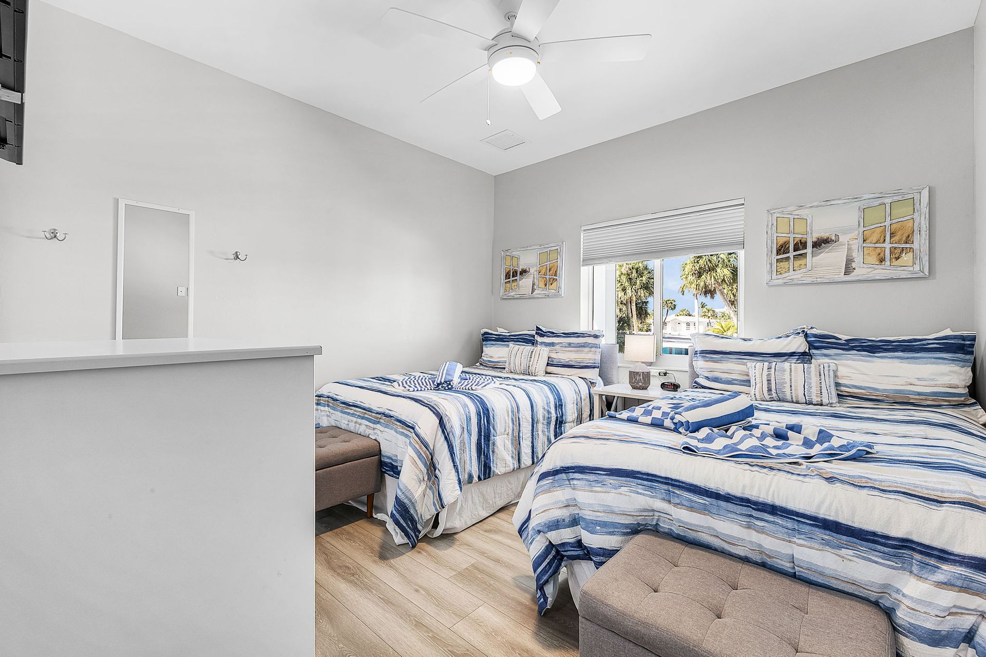 Bright bedroom with three blue-and-white striped beds, white walls, and a ceiling fan by a window