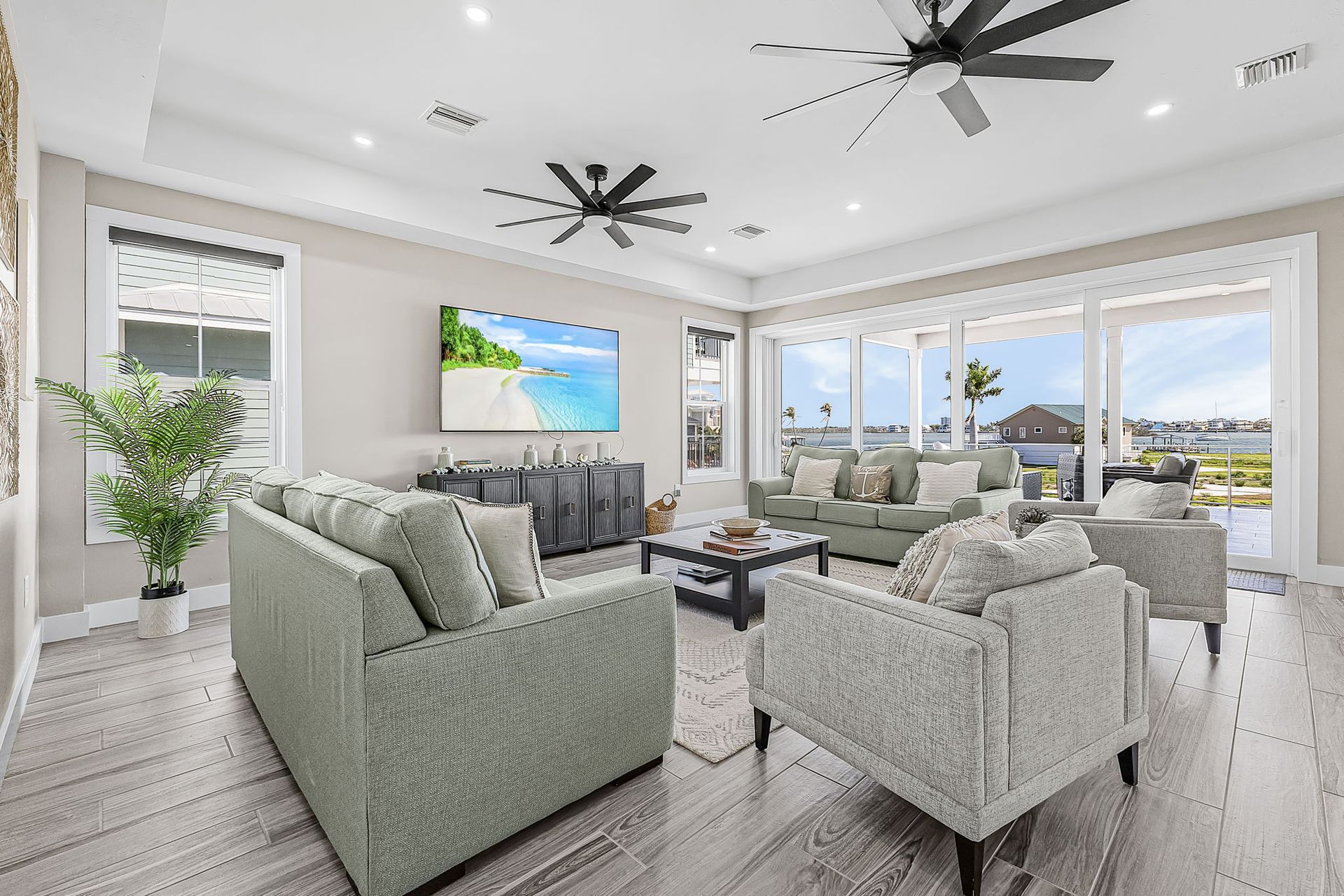 Bright modern living room with gray sofas, ceiling fans, large windows, and ocean views