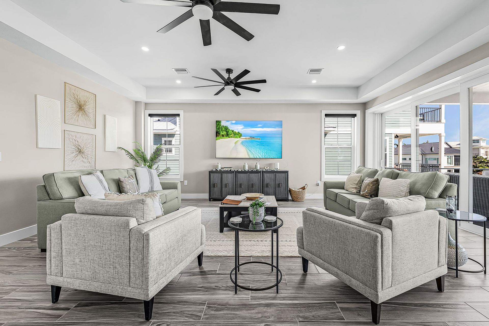 Bright modern living room with gray sofas, ceiling fans, and a TV above the fireplace.