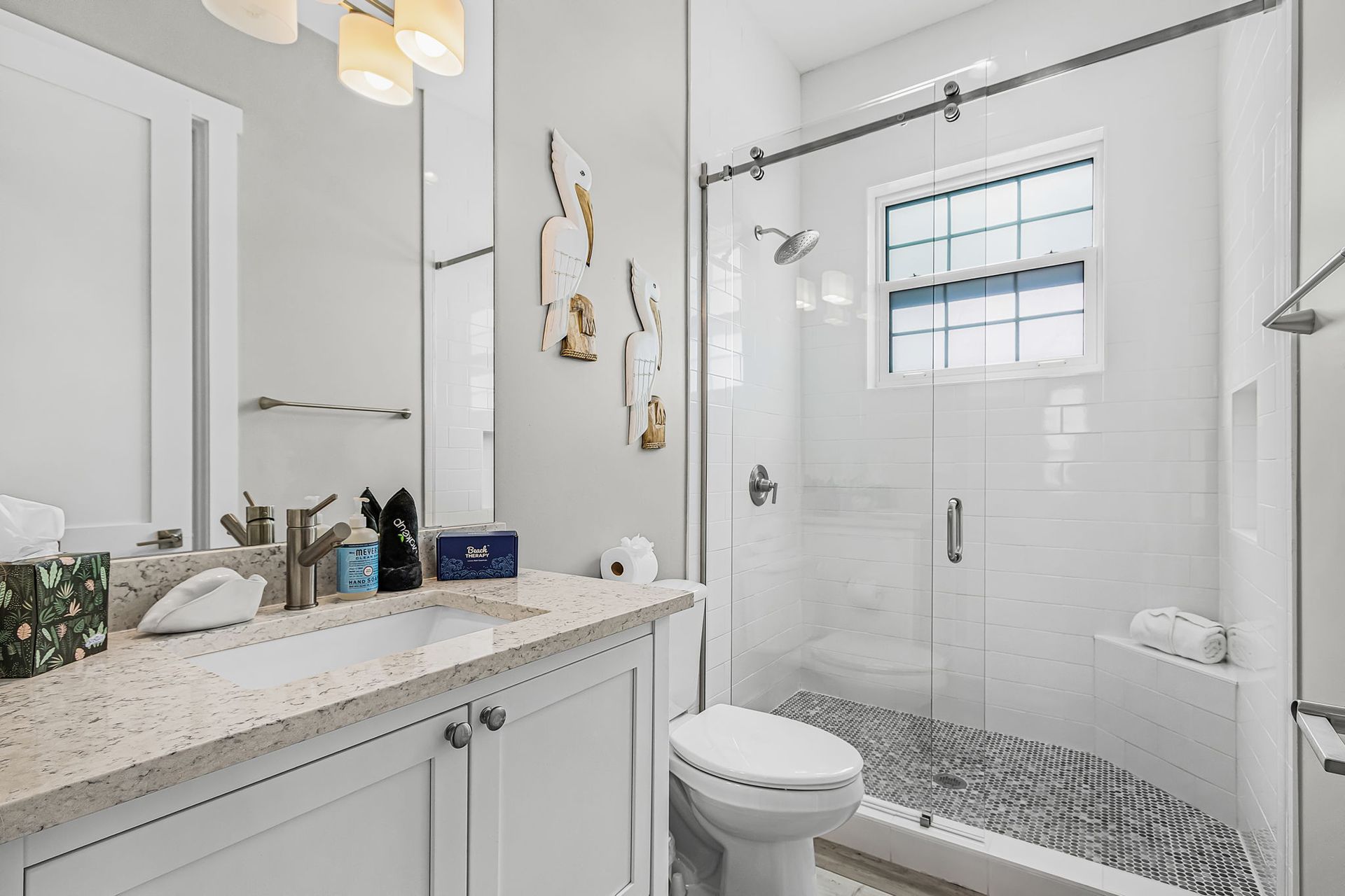Bright white bathroom with vanity, mirror, toilet, glass shower, and patterned tile floor.