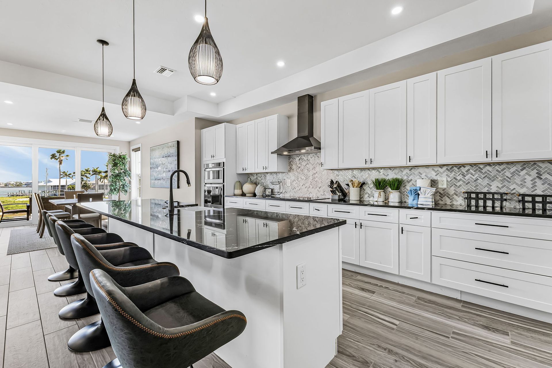 Bright modern kitchen with white cabinets, black island, pendant lights, and bar stools overlooking a dining area.