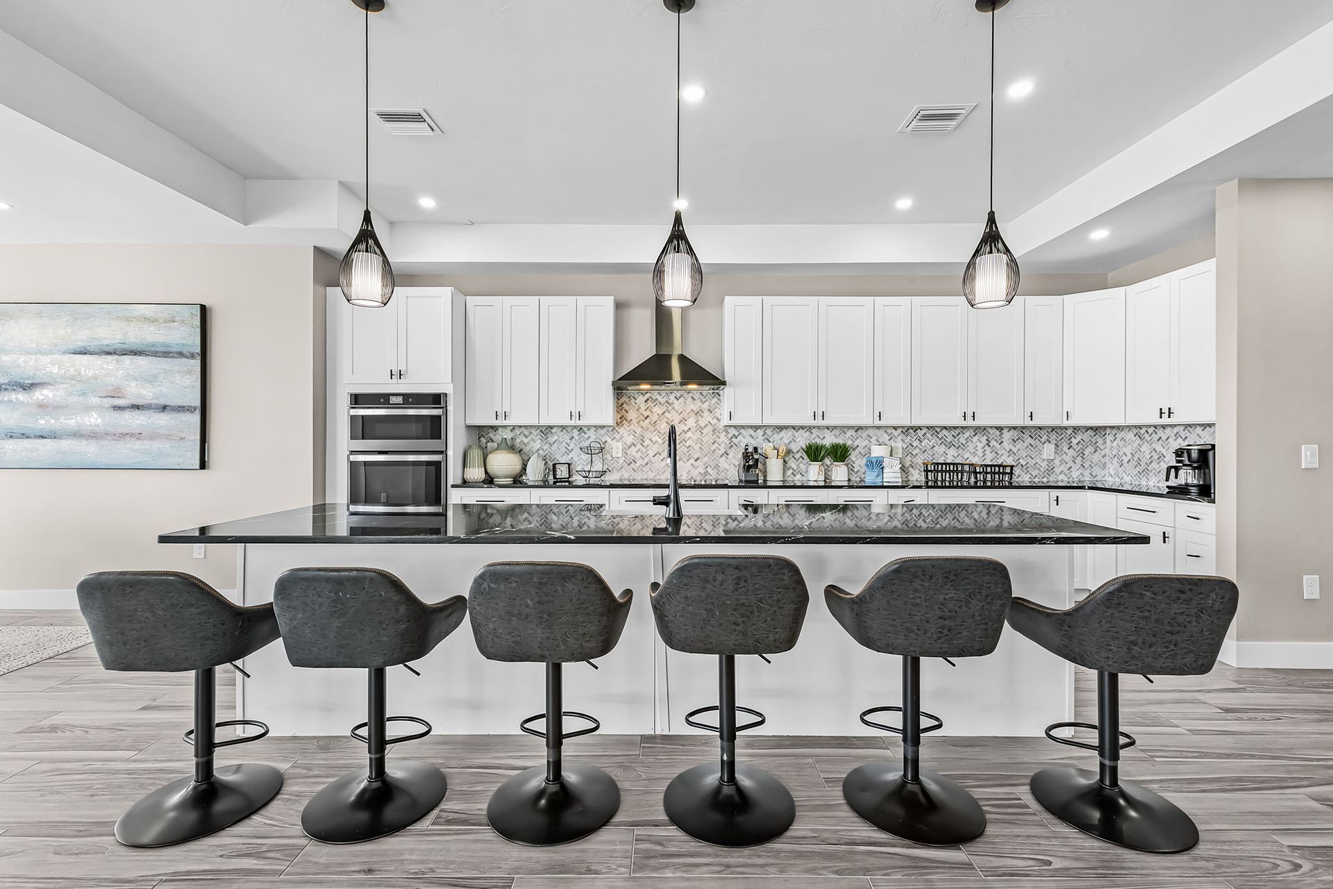 Modern white kitchen with granite island, five black barstools, and three pendant lights