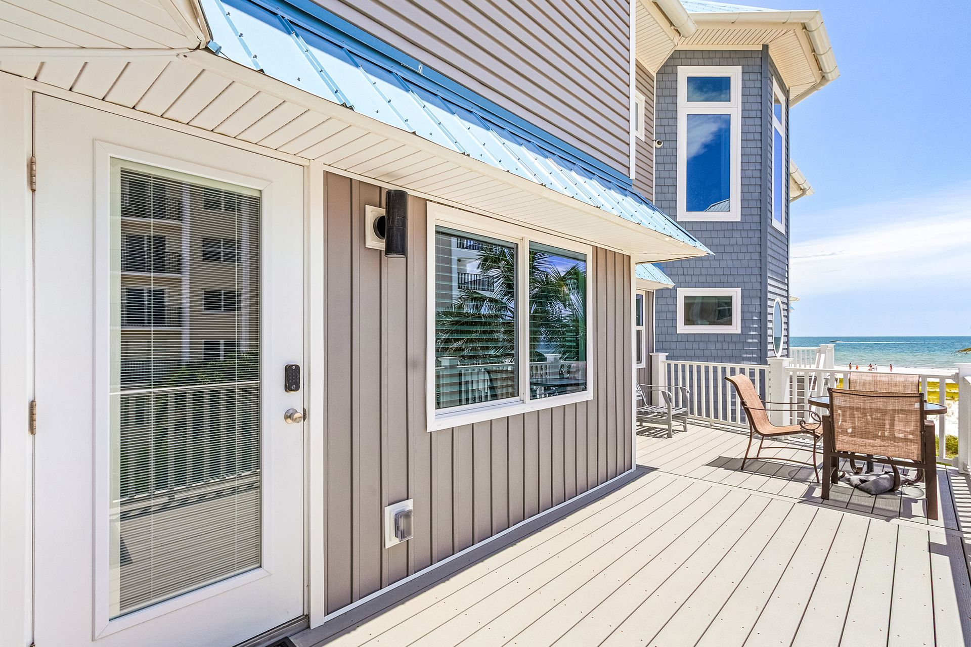 Beachfront deck beside a gray house with white trim, ocean view, and outdoor seating