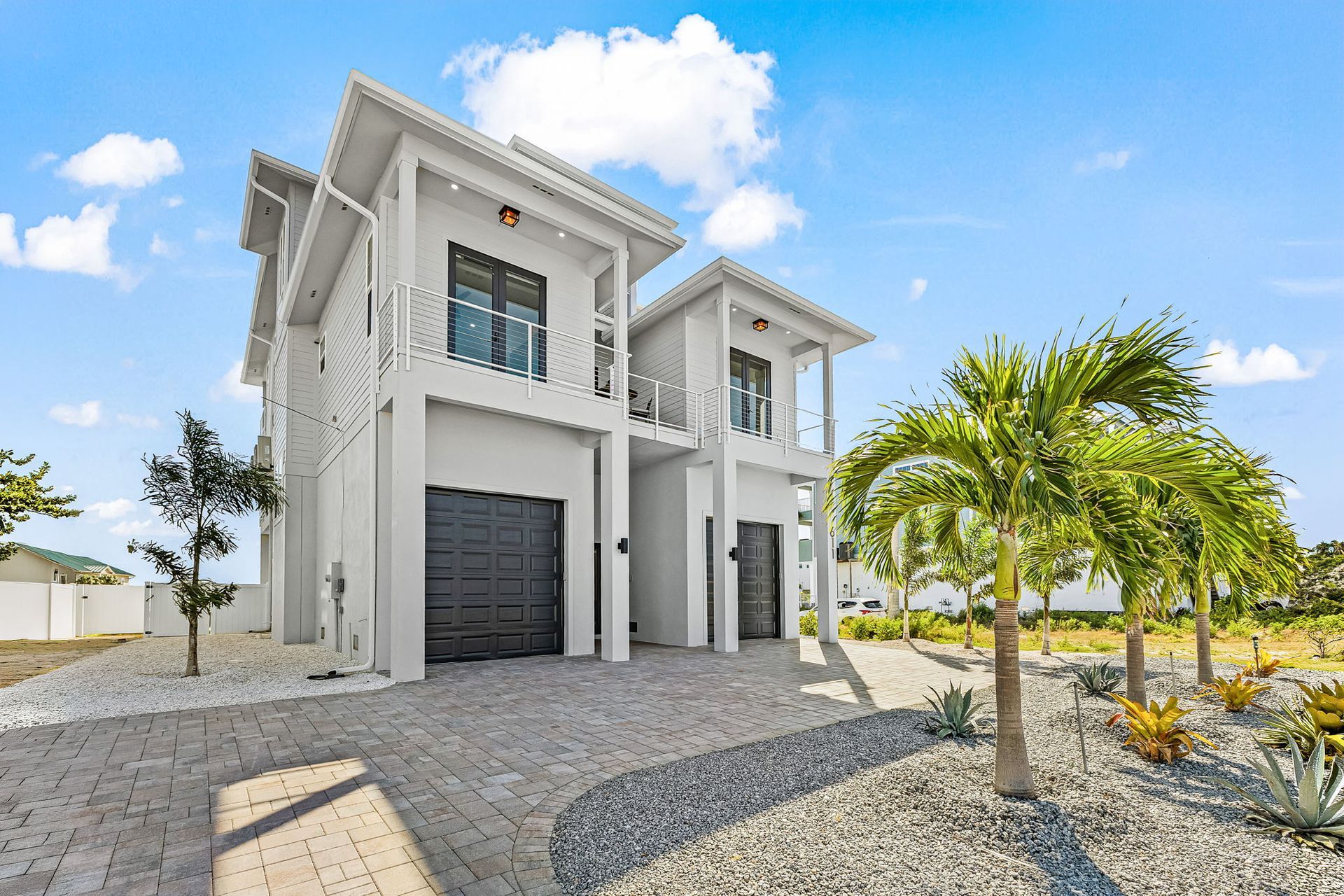Modern two-story white house with palm trees and gravel driveway under a bright blue sky