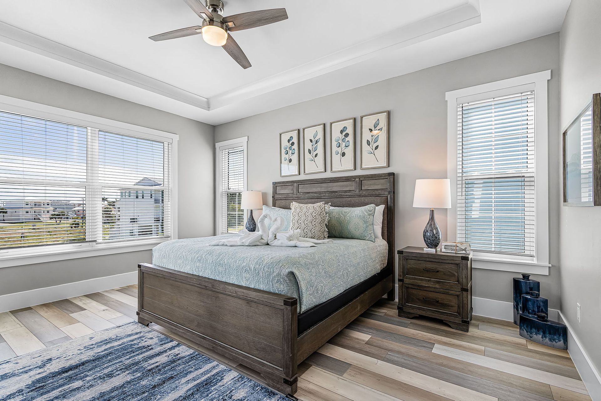 Bright bedroom with a dark wood bed, blue-gray decor, large windows, and a ceiling fan