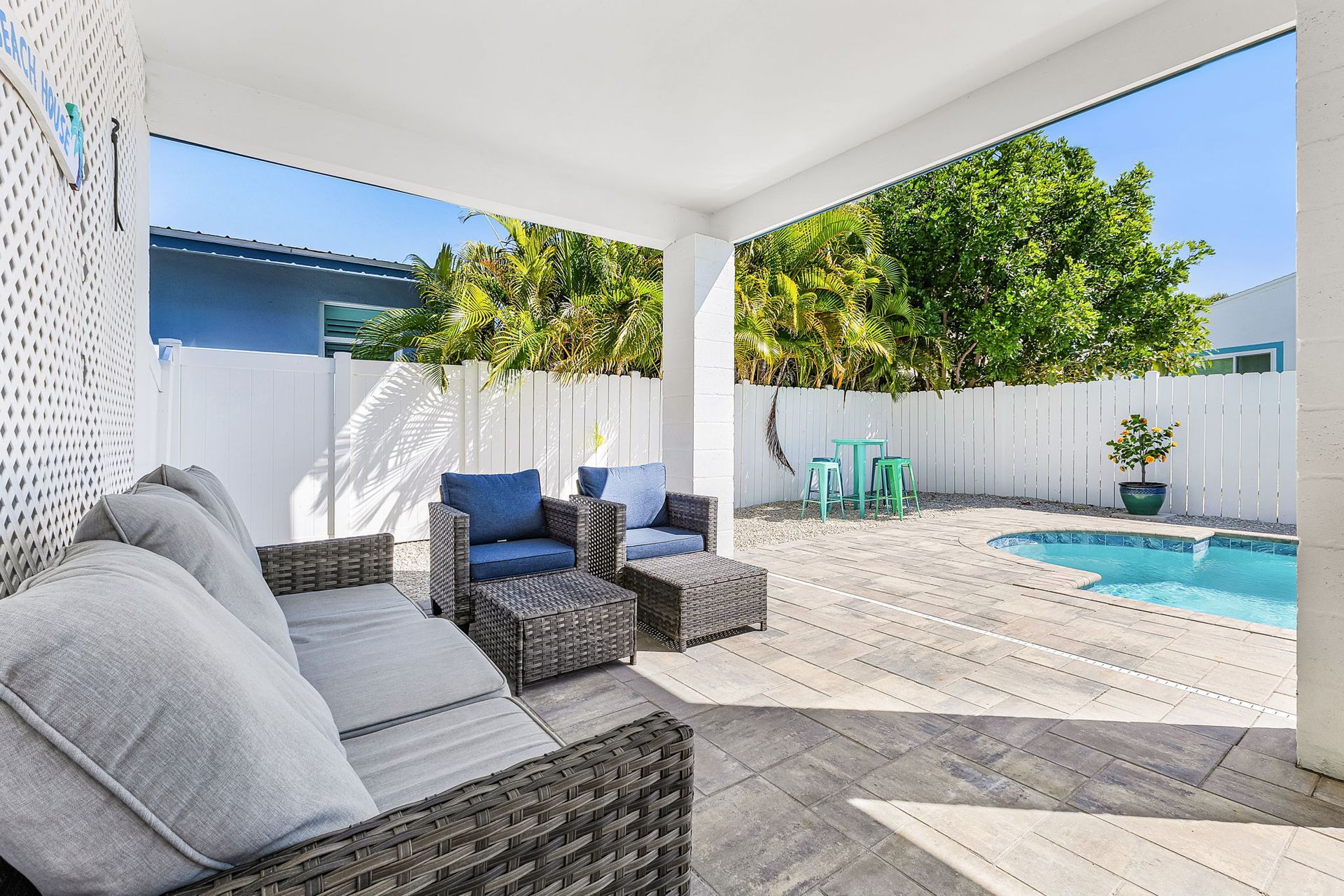 Covered patio with wicker chairs overlooking a small backyard pool and white privacy fence