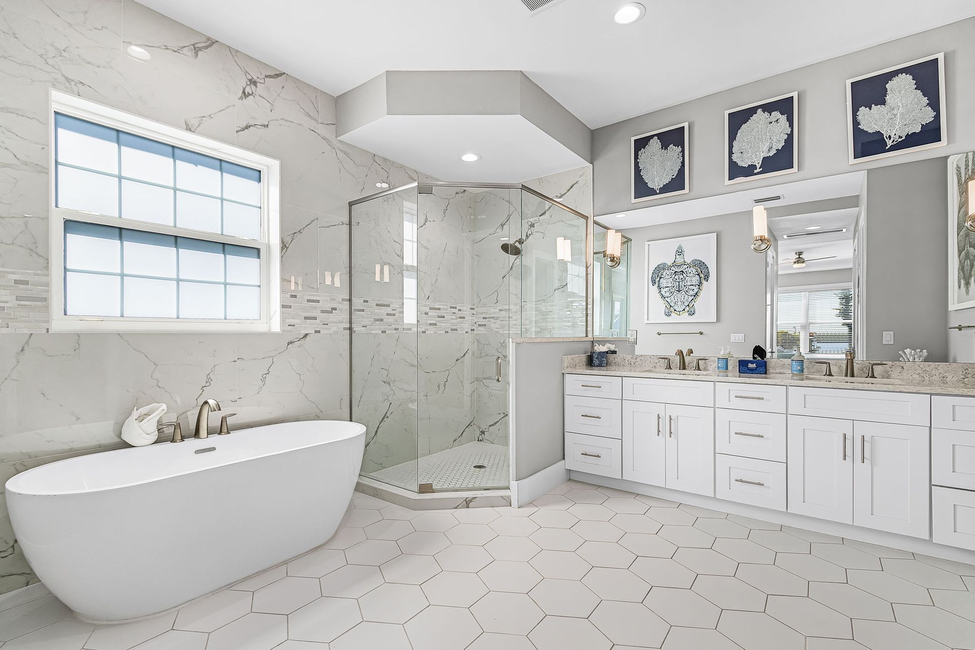Bright modern bathroom with freestanding tub, glass shower, double vanity, and white hex tile floor