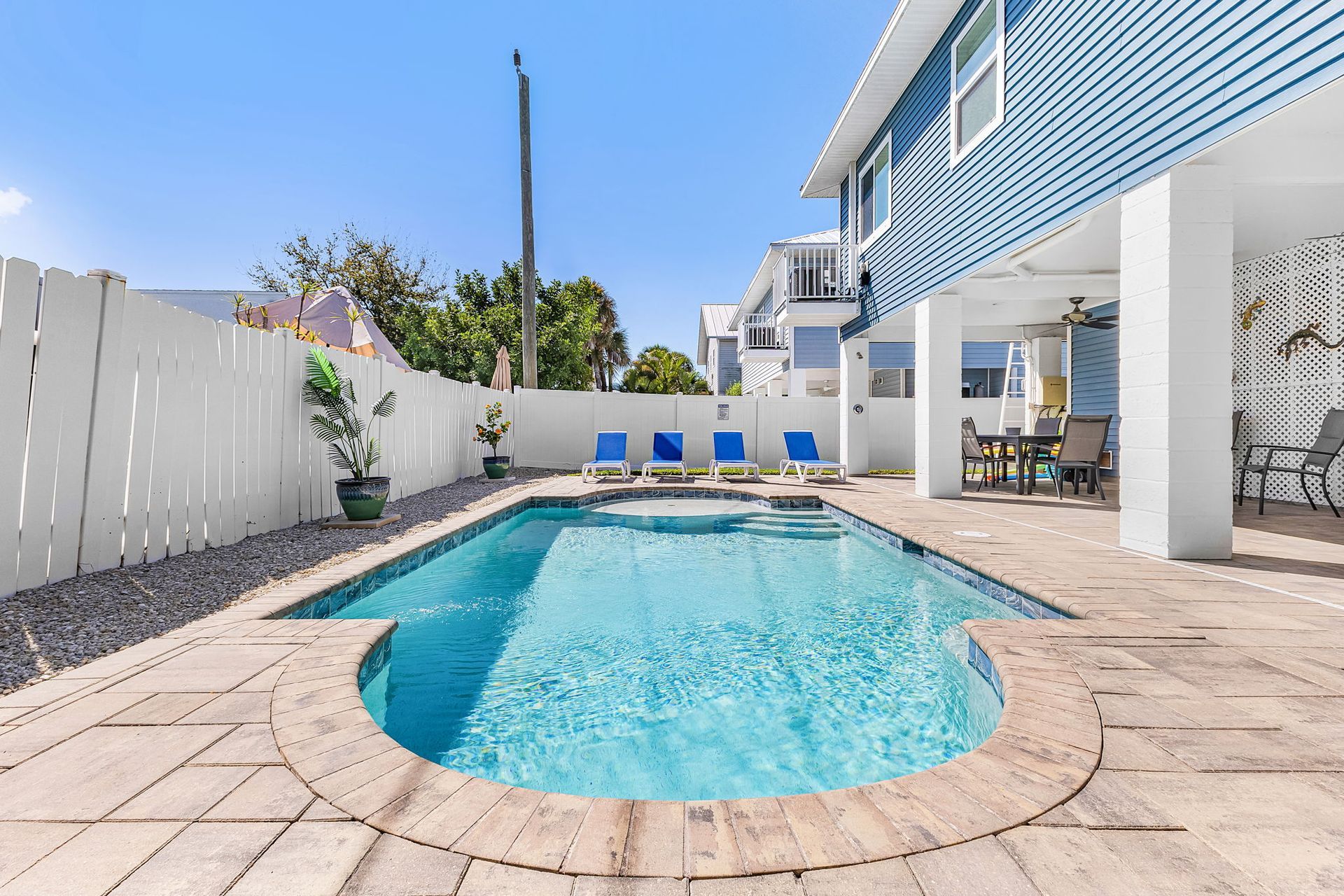 Backyard swimming pool with blue lounge chairs and white fence beside a house