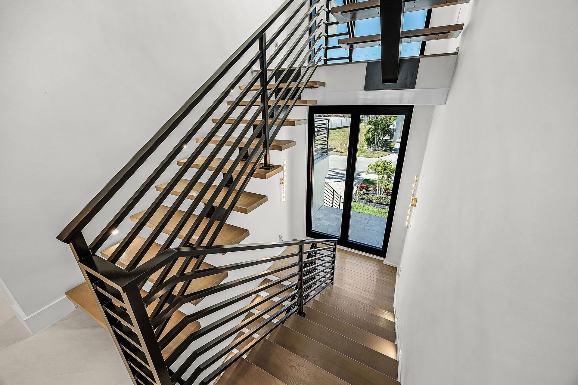Staircase with wooden steps and black metal railings leading to a glass door.