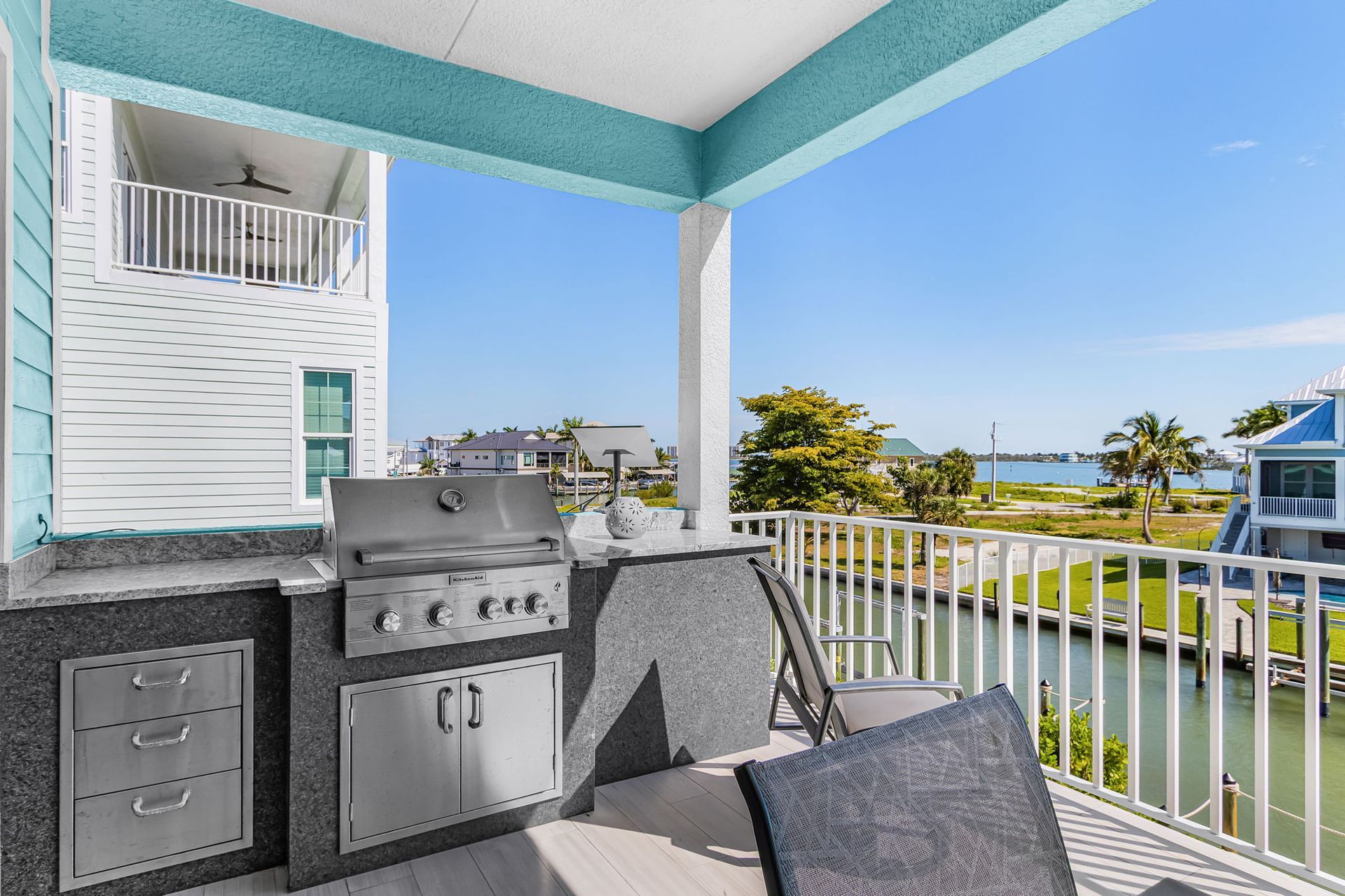 Balcony with grill and chairs overlooking water and neighboring homes