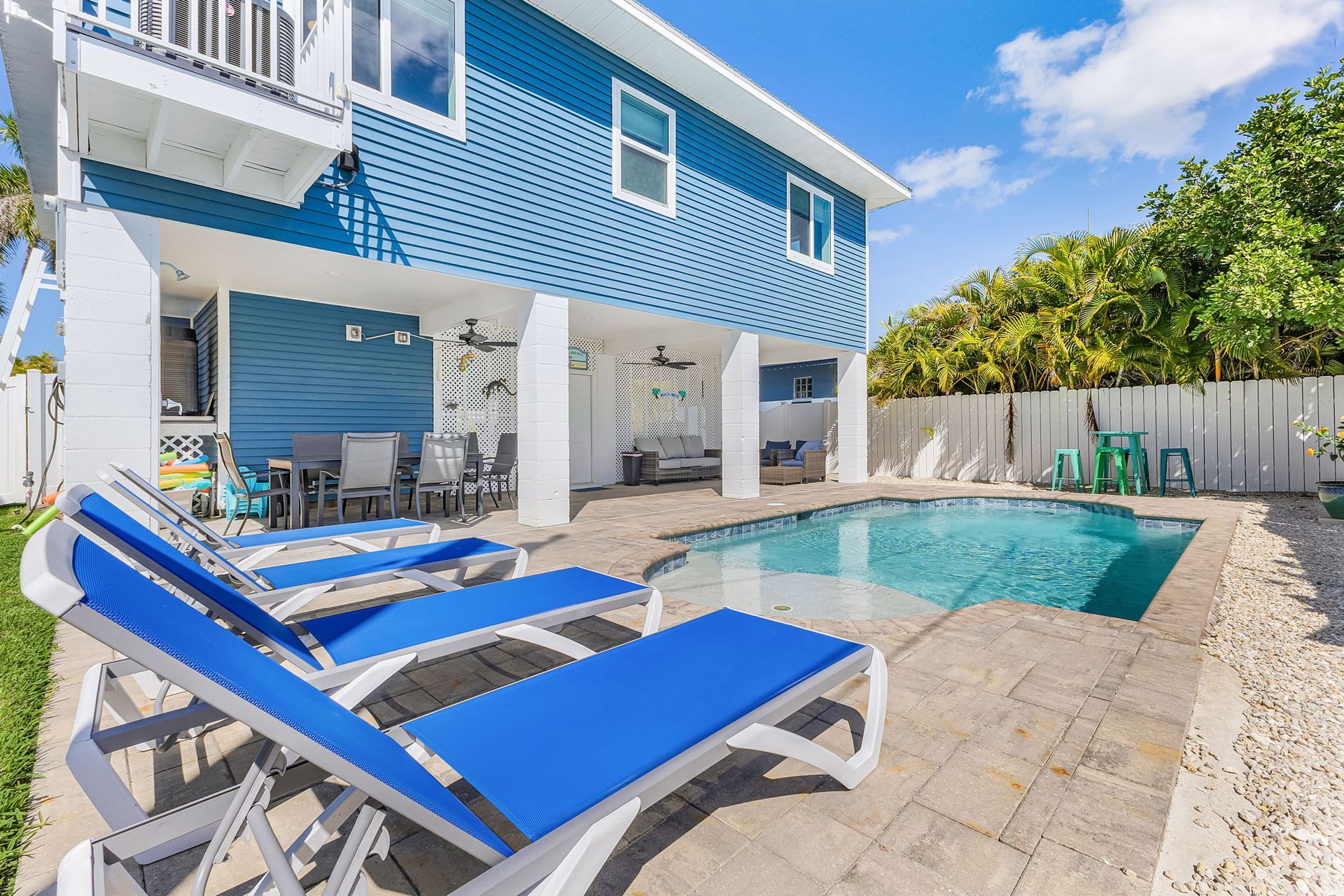 Blue lounge chairs by a backyard pool beside a blue house and white pergola