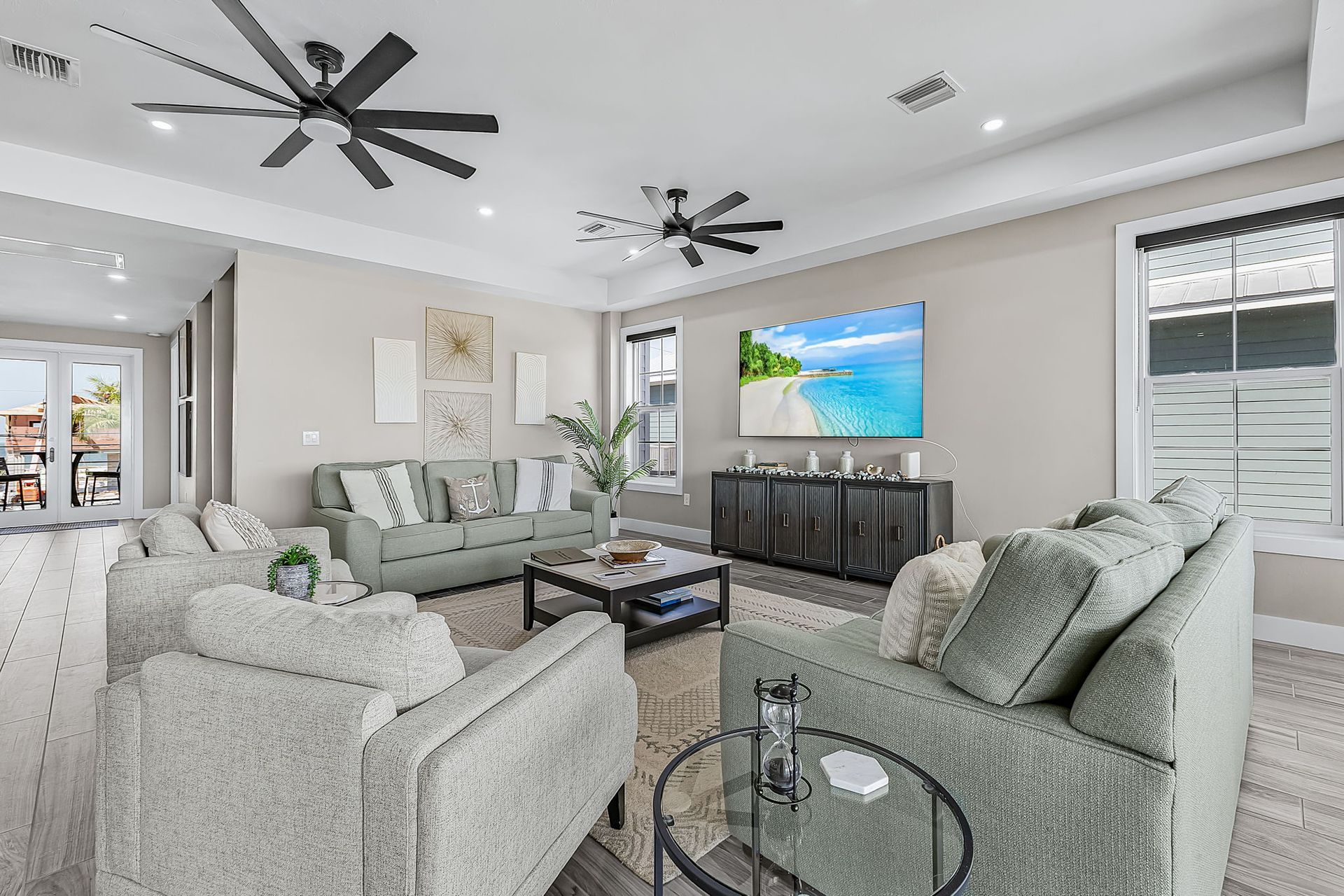 Bright living room with light gray sofas, glass coffee table, ceiling fans, and a TV on a dark console.