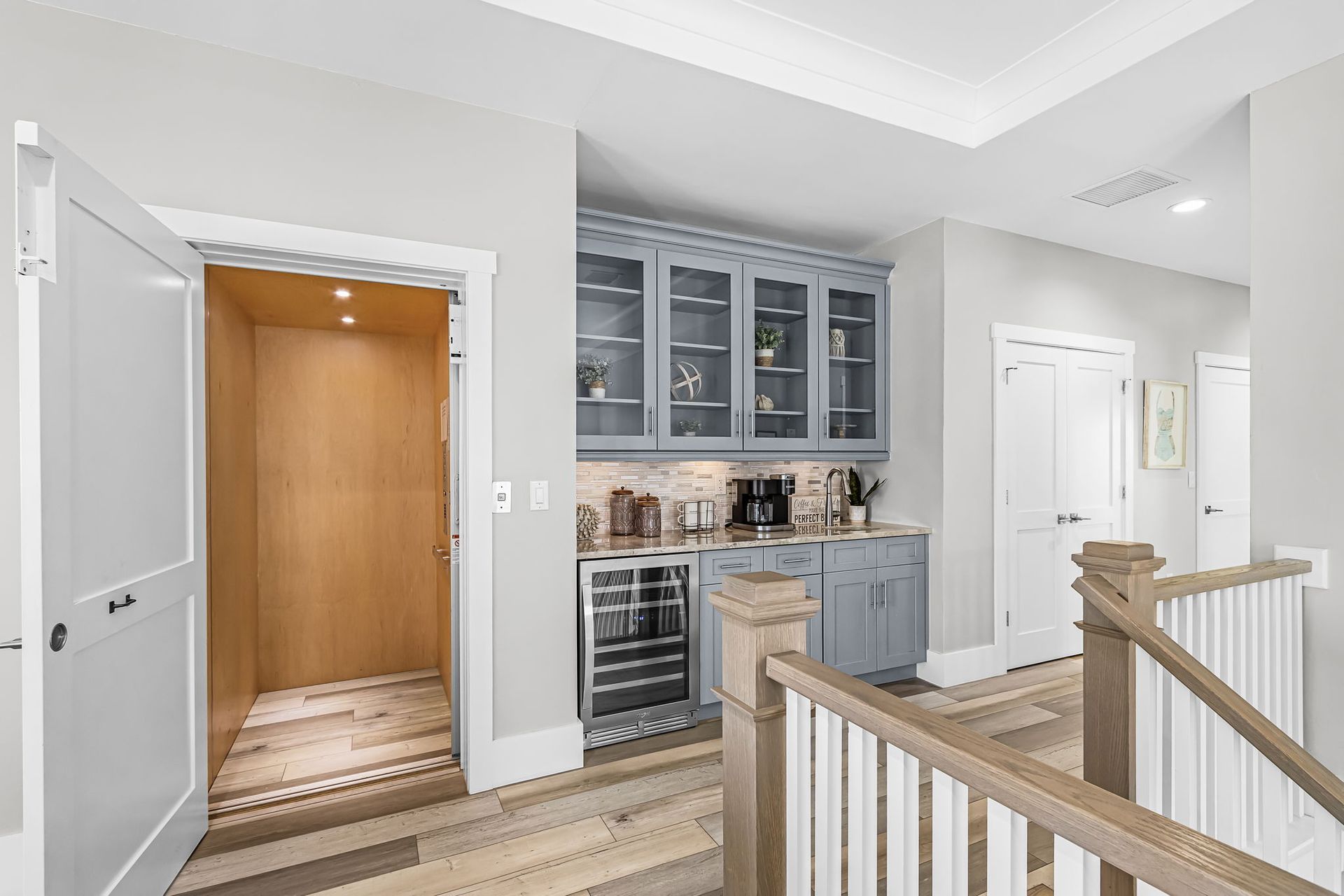 Bright hallway with open closet, built-in cabinets, and wooden stairs railing in a modern home