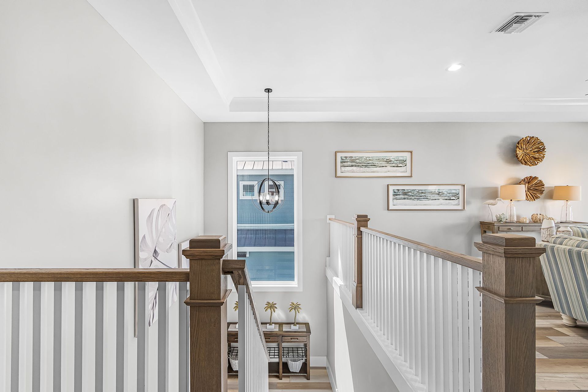 Bright upstairs hallway with white railings, wooden posts, and framed wall art overlooking a stairwell.