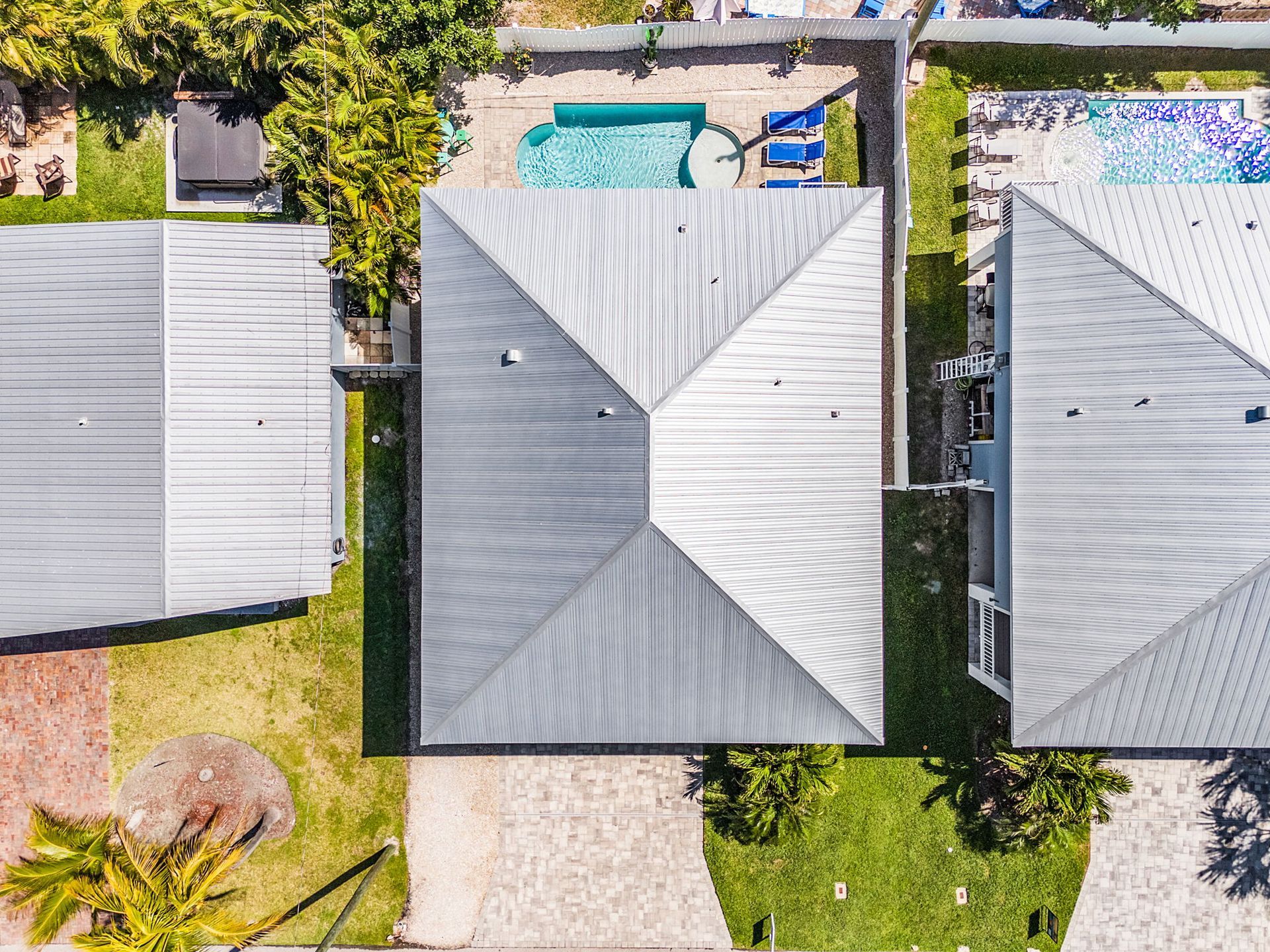 Aerial view of three gray-roofed houses with yards and a swimming pool.