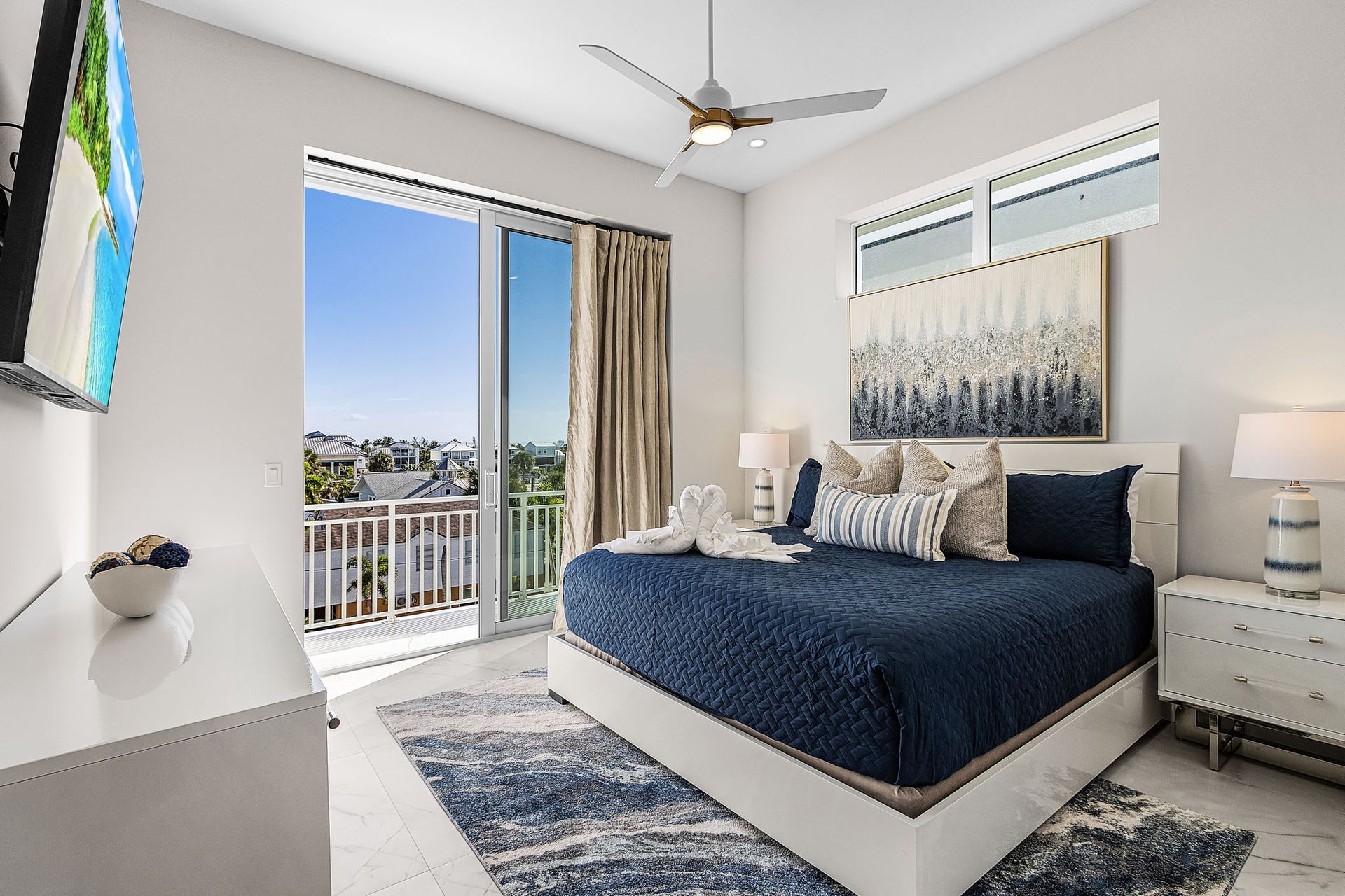 Bedroom with a blue bed, balcony, and a painting; white walls and a blue rug.