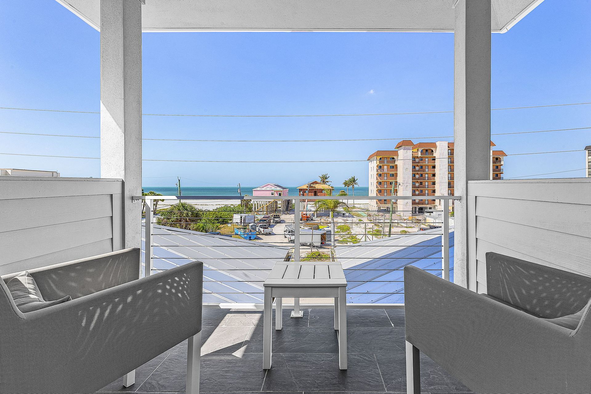 Balcony seating with ocean view, blue sky, and resort buildings in the distance