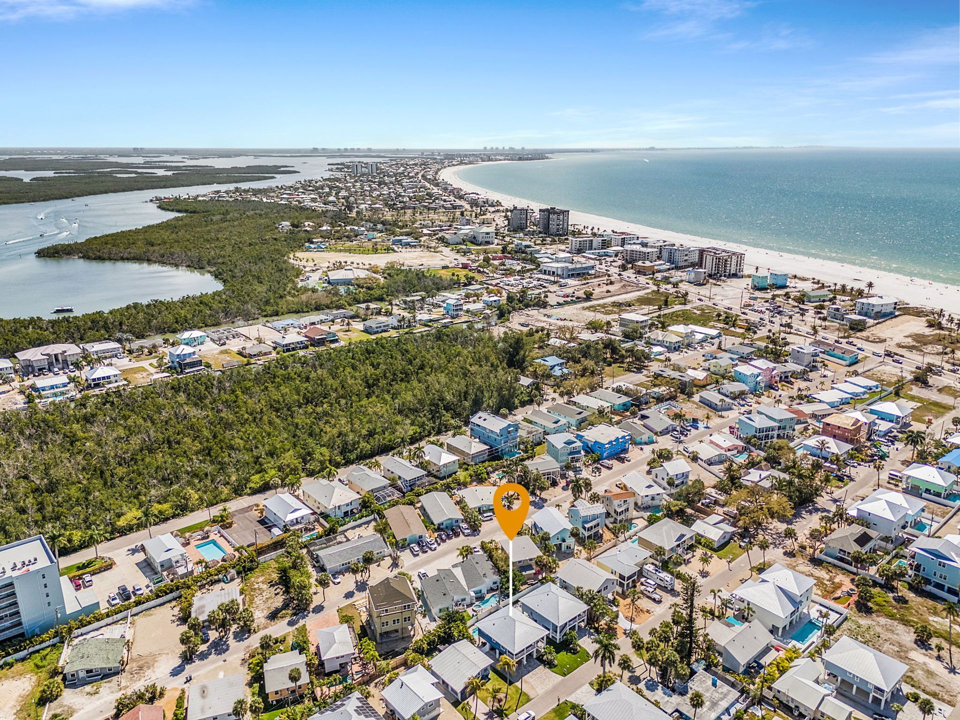 Aerial view of a coastal neighborhood with houses, palm trees, and a sandy beach along blue ocean water