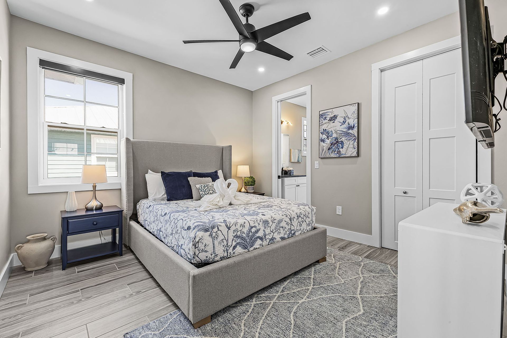 Modern gray bedroom with bed, ceiling fan, window, dresser, and patterned rug
