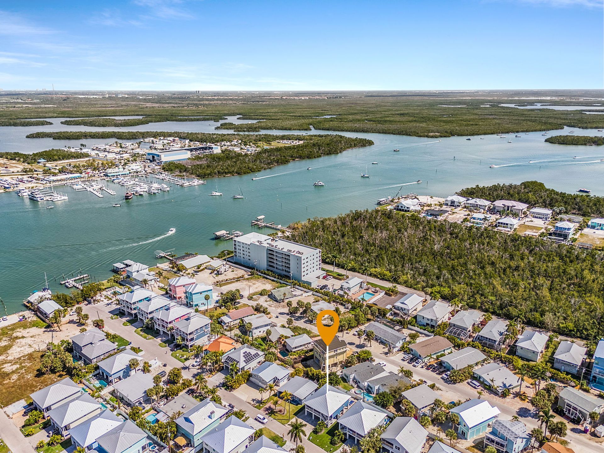 Aerial view of coastal neighborhood with boats, canals, and waterfront homes under a blue sky