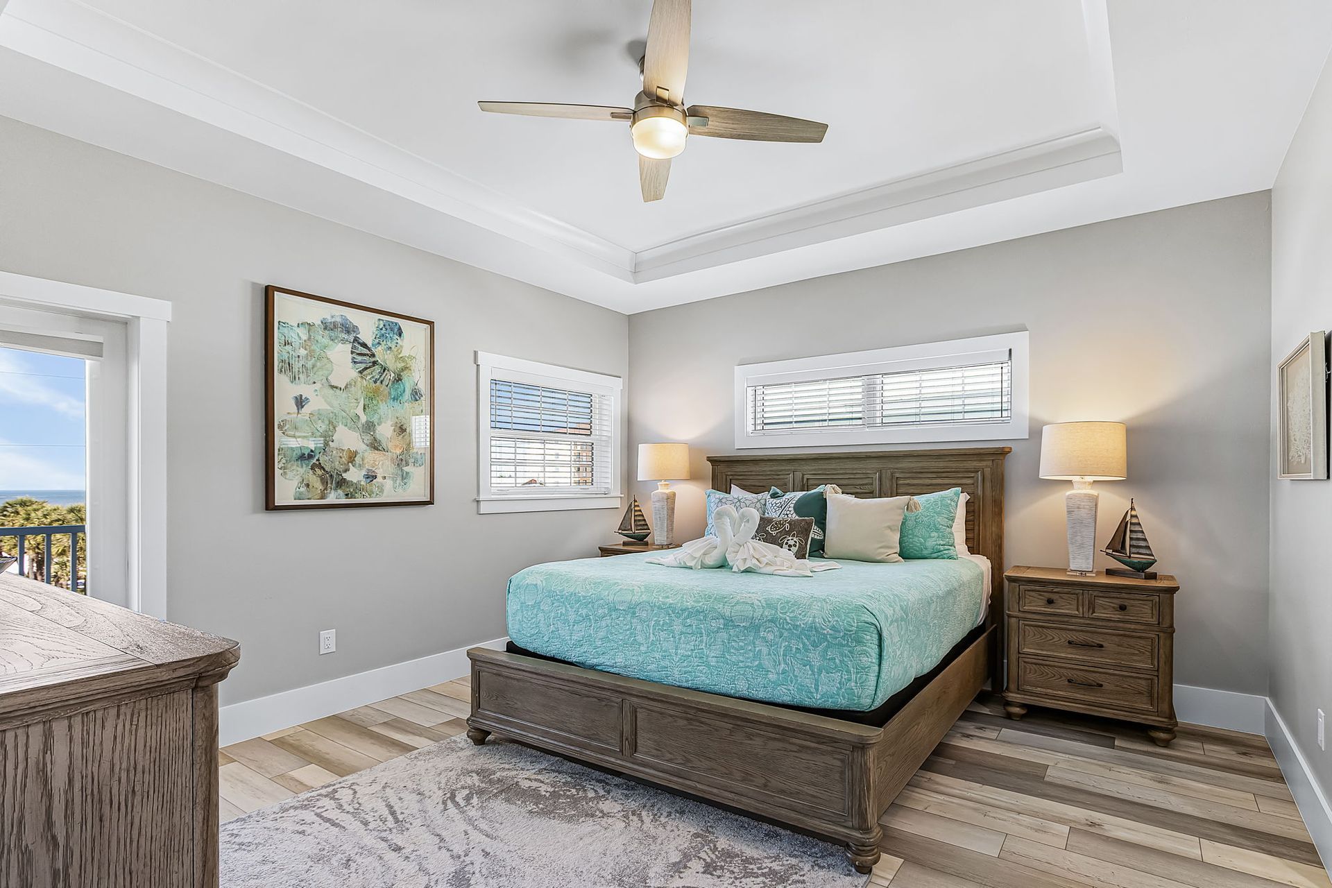 Bright bedroom with aqua bedding, gray walls, ceiling fan, nightstands, and patterned rug