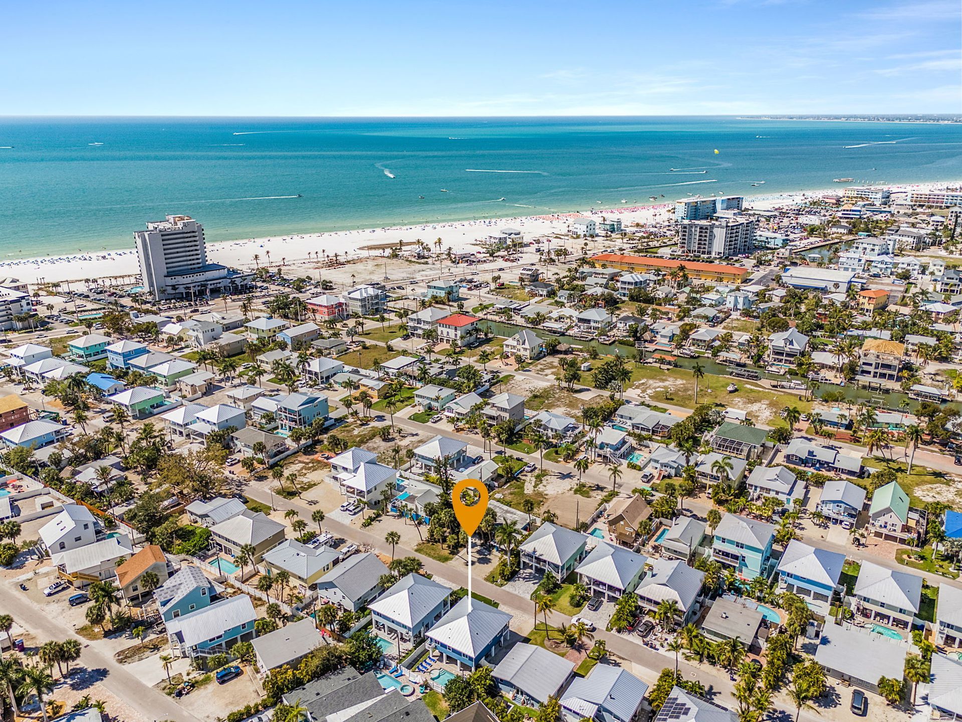 Aerial view of a coastal neighborhood with beach, turquoise ocean, and dense houses under a clear sky