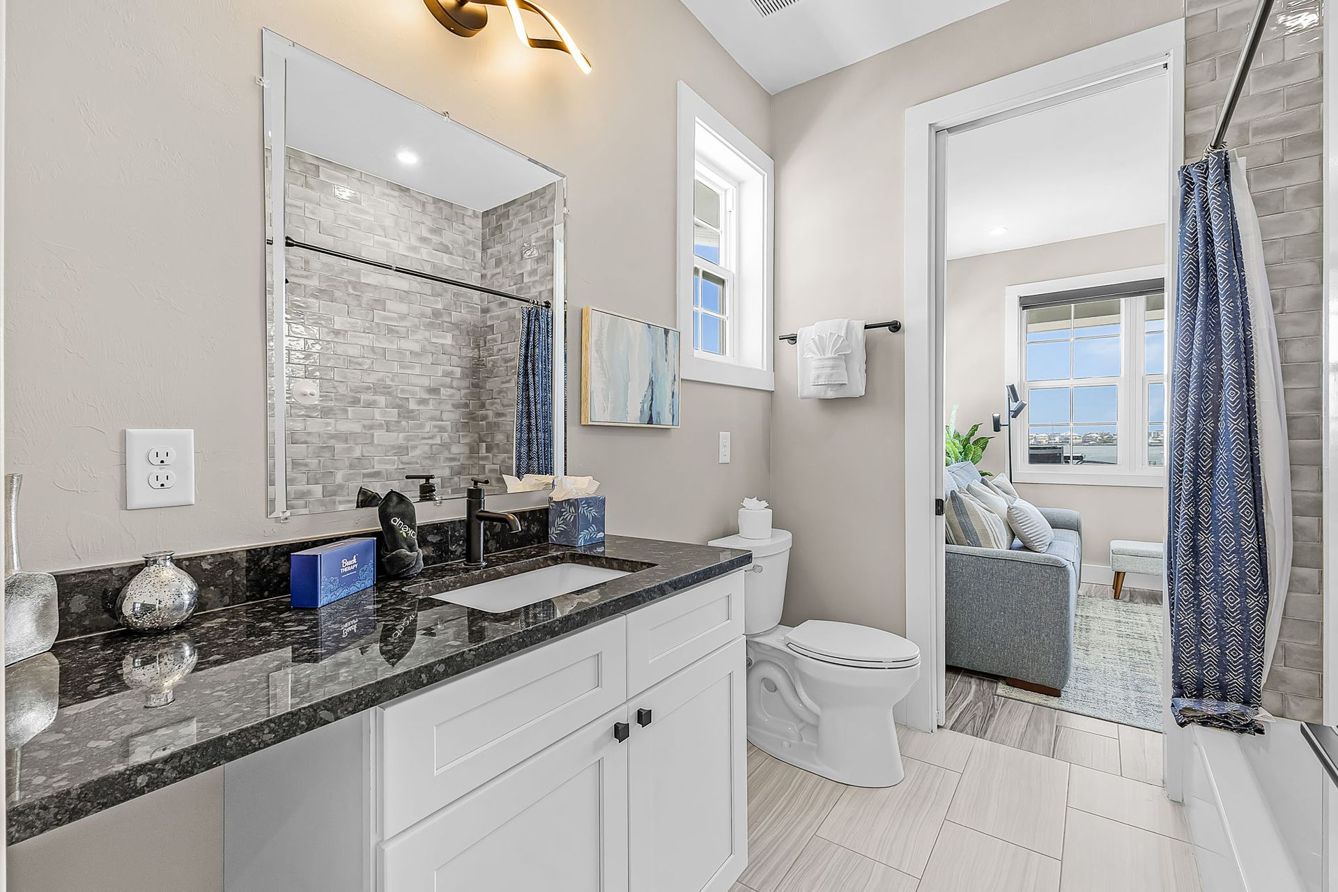 Bright bathroom with white vanity, black countertop, large mirror, and tub with mosaic tile surround.