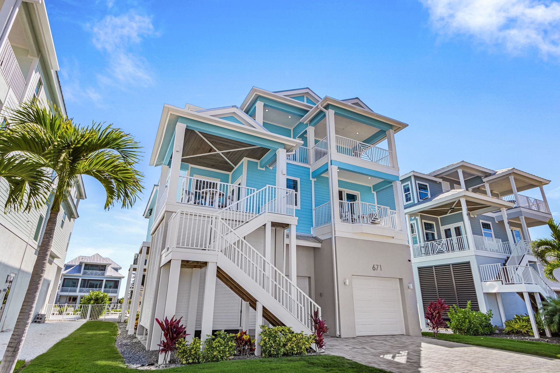 White coastal stilt house with blue accents and a wraparound stairway under a bright blue sky
