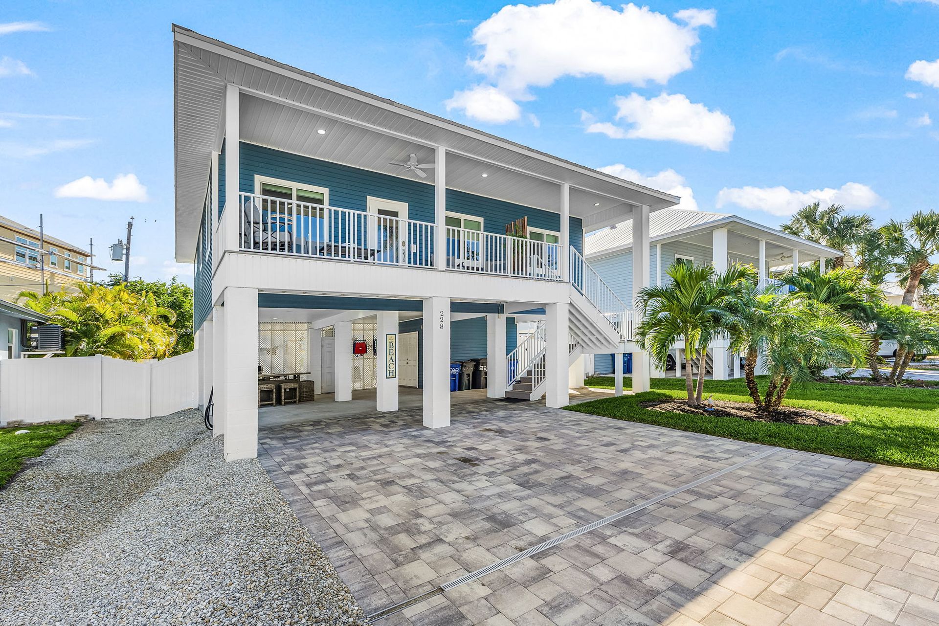 Modern two-story house with white trim, balcony, driveway, and landscaped yard under a blue sky