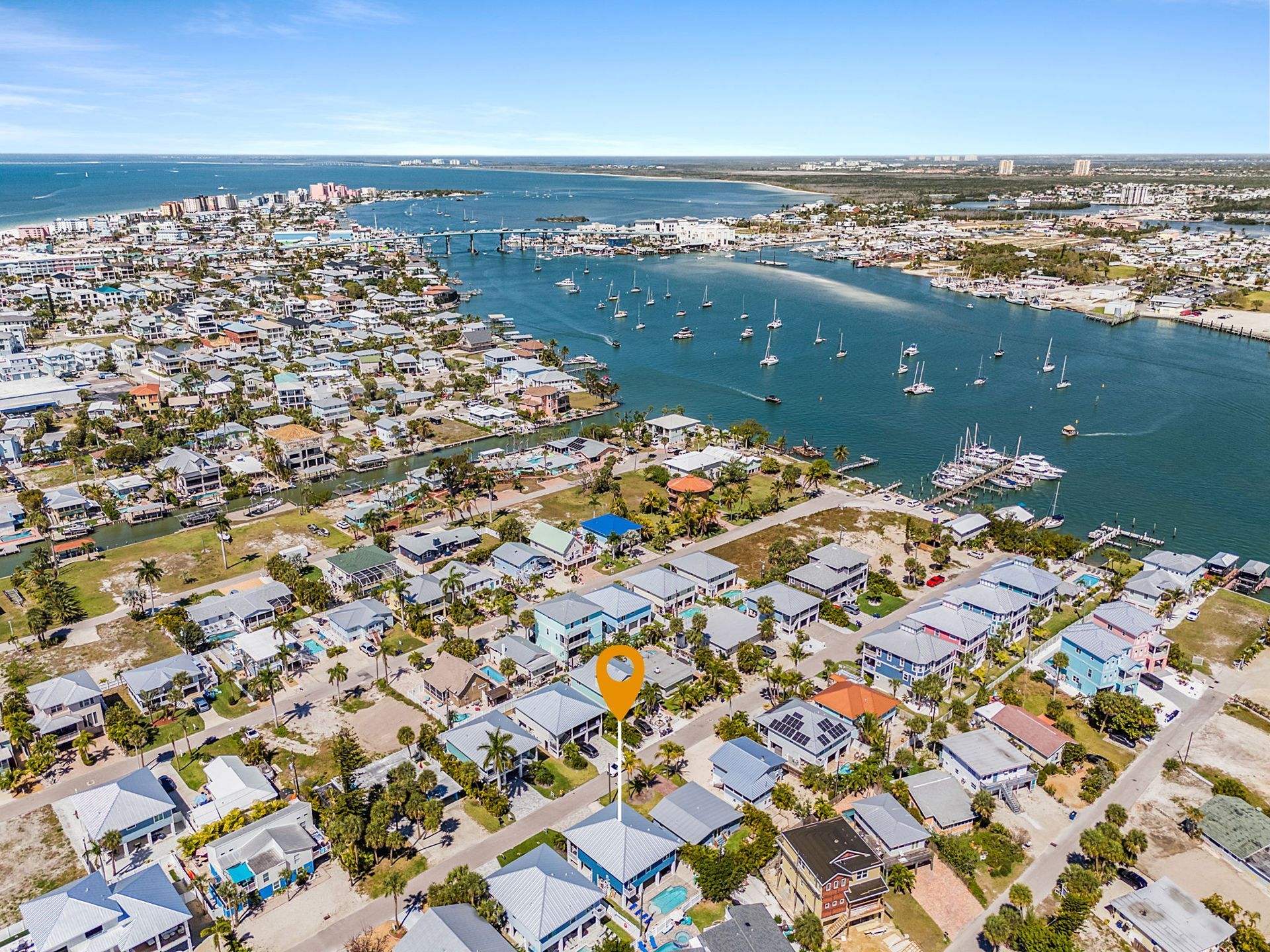 Aerial view of a coastal neighborhood with boats in a blue waterway and the ocean beyond.