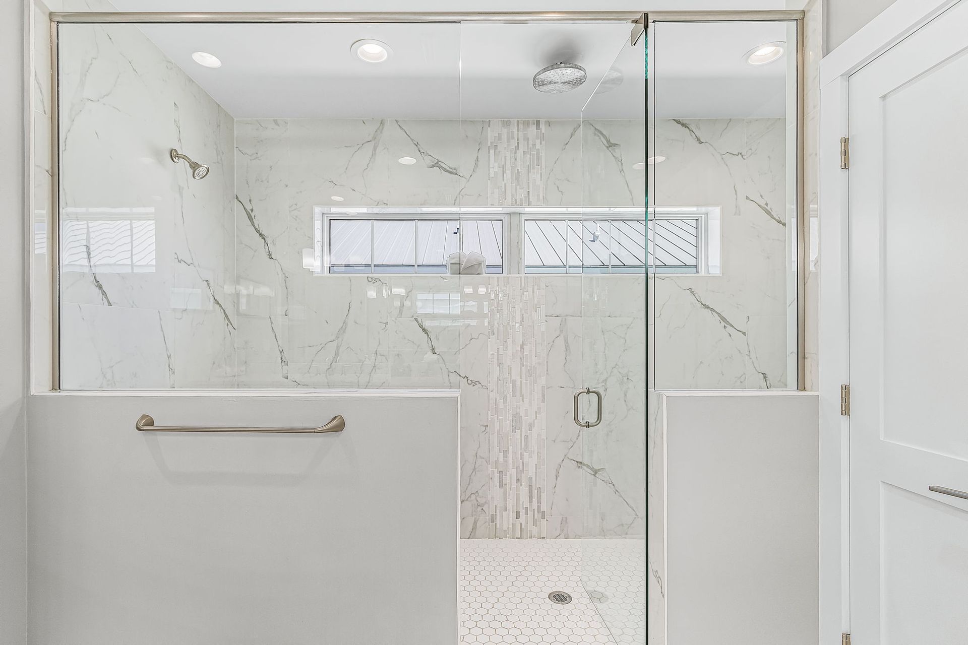 Bright white tiled bathroom with a glass shower enclosure and frosted window.