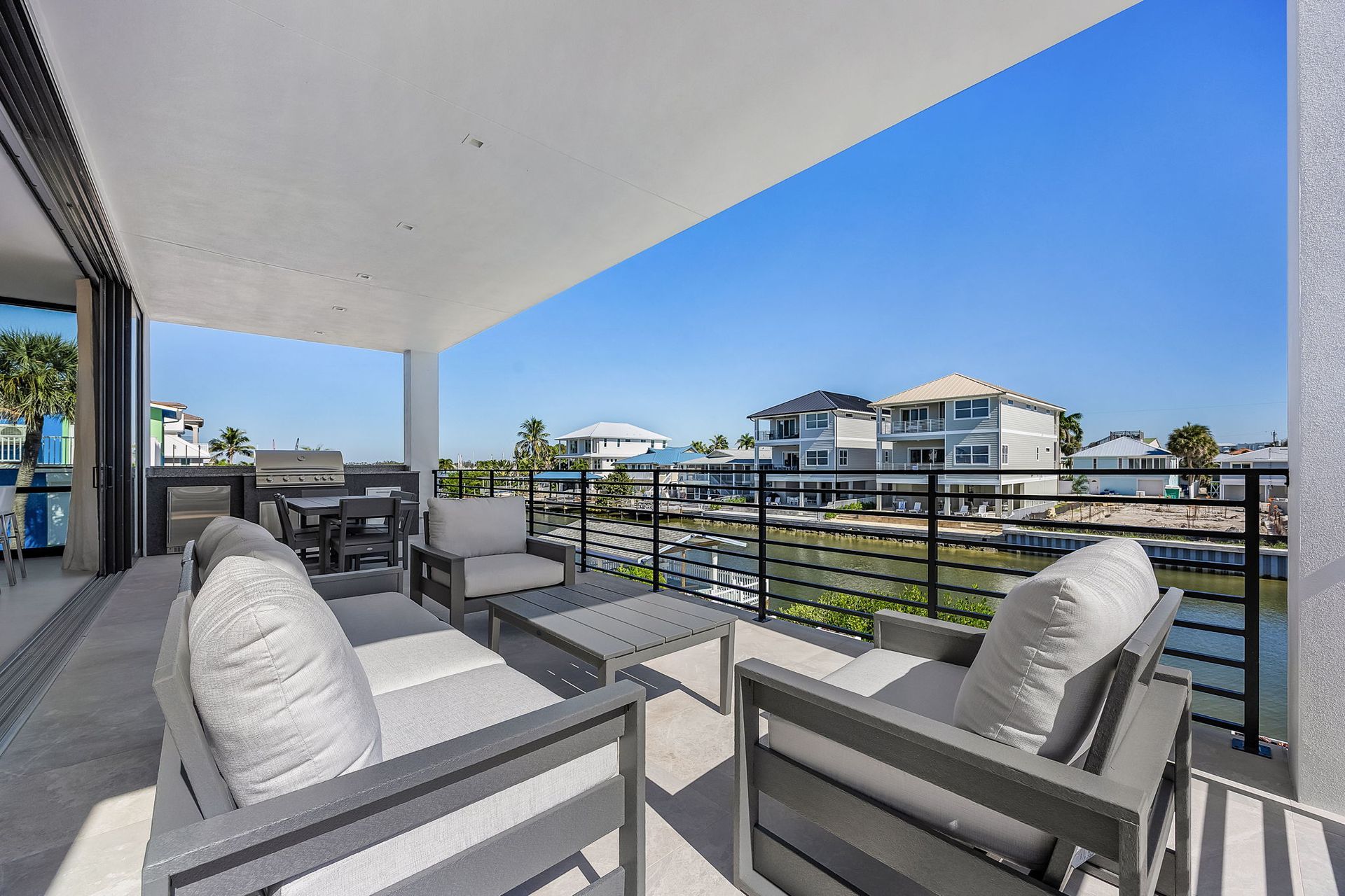 Patio with gray furniture, overlooking a canal with houses on a sunny day.
