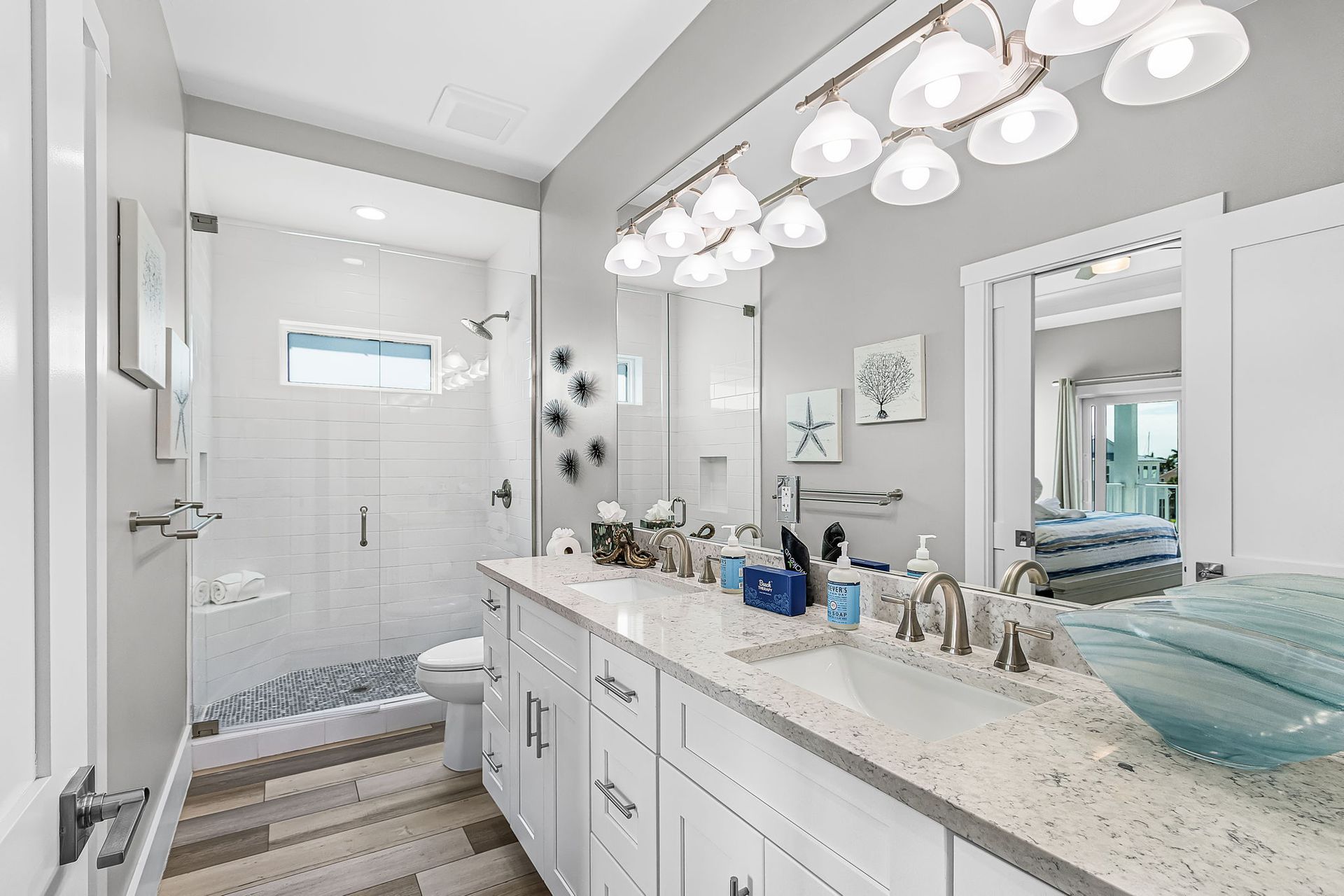 Bright white bathroom vanity with double sinks, large mirror, and glass-enclosed shower in back