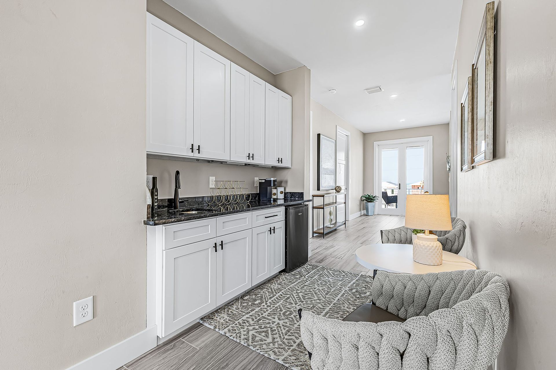 Bright hallway with white kitchen cabinets, granite counter, gray chair, and lamp in a modern apartment