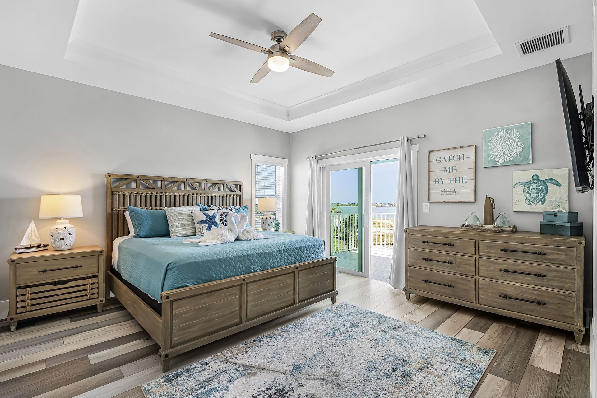 Bright bedroom with a wooden bed, dresser, blue bedding, and open doors to a balcony.