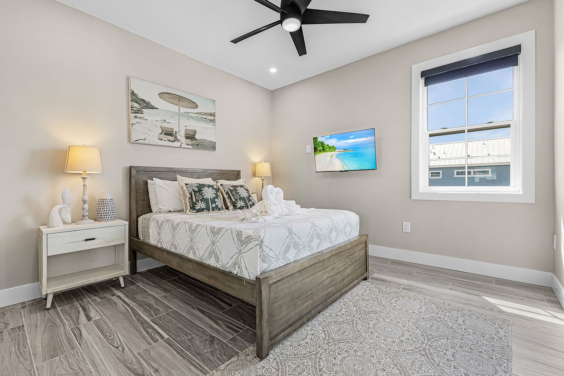 Bright bedroom with bed, bedside tables, lamps, wall art, gray rug, and window with view.