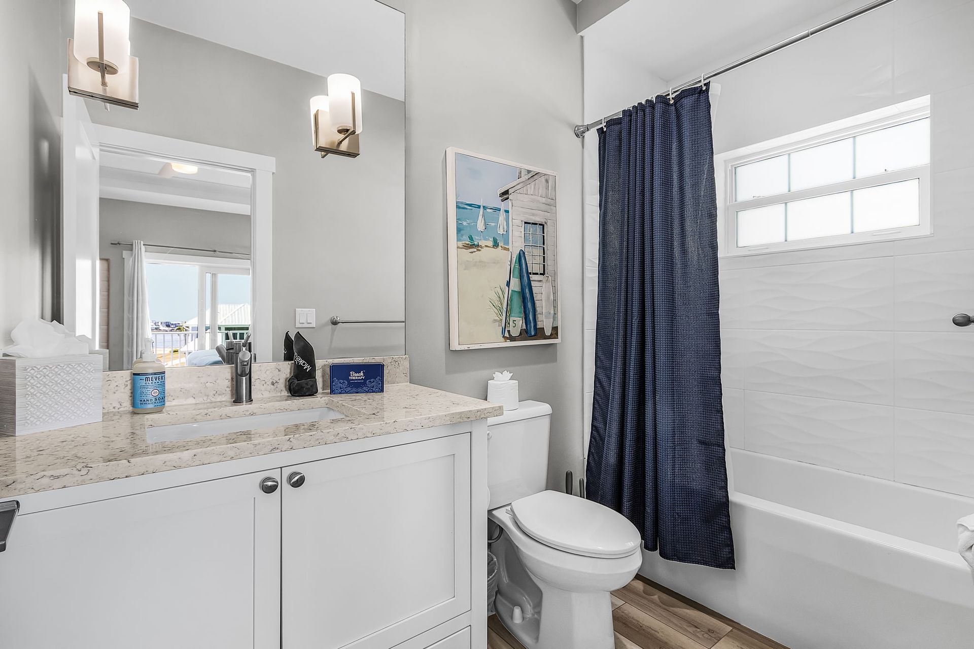 Bright bathroom with white vanity, mirror, toilet, shower curtain, and tub