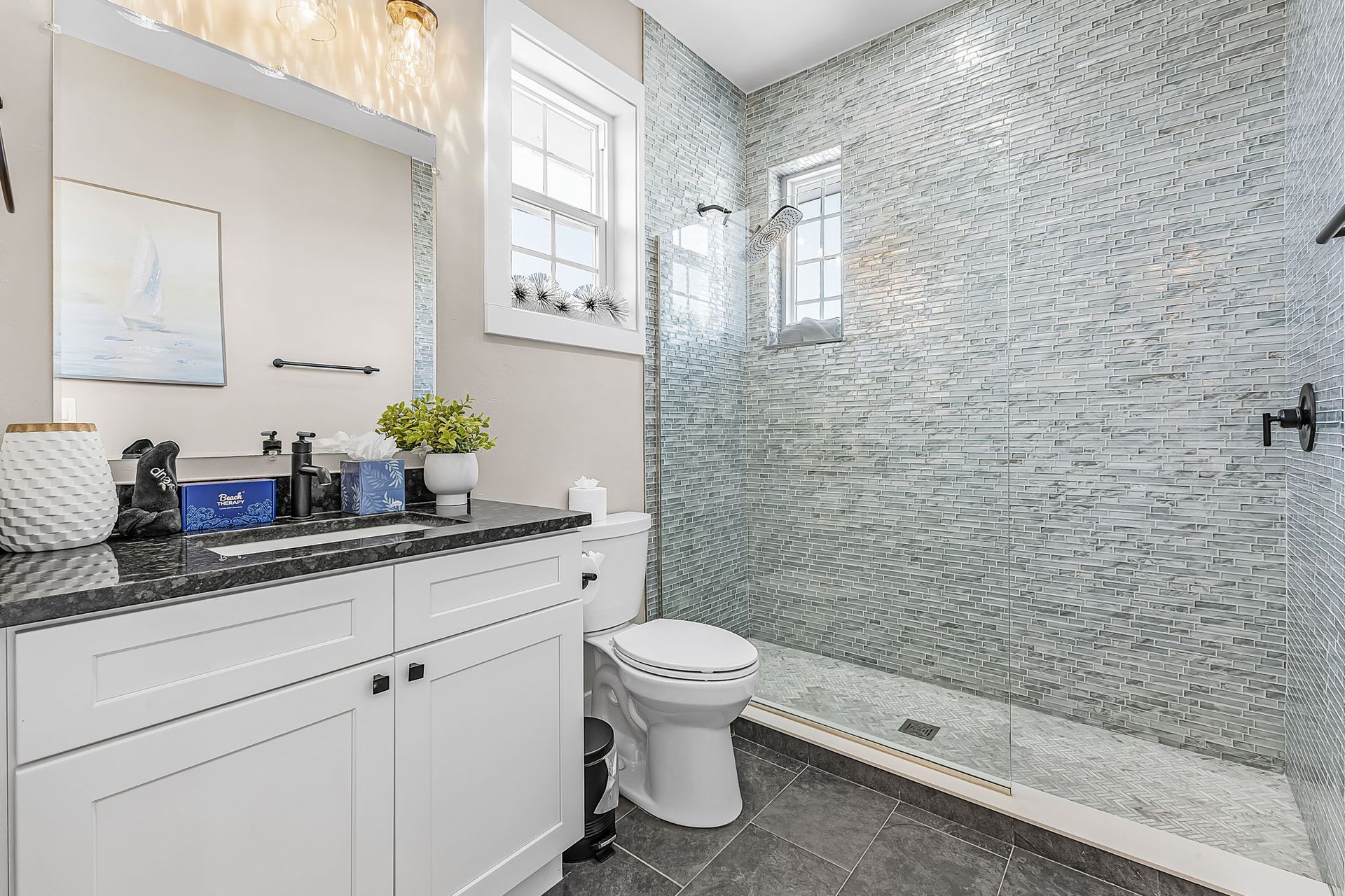 Bright modern bathroom with white vanity, speckled countertop, toilet, and glass shower wall￼