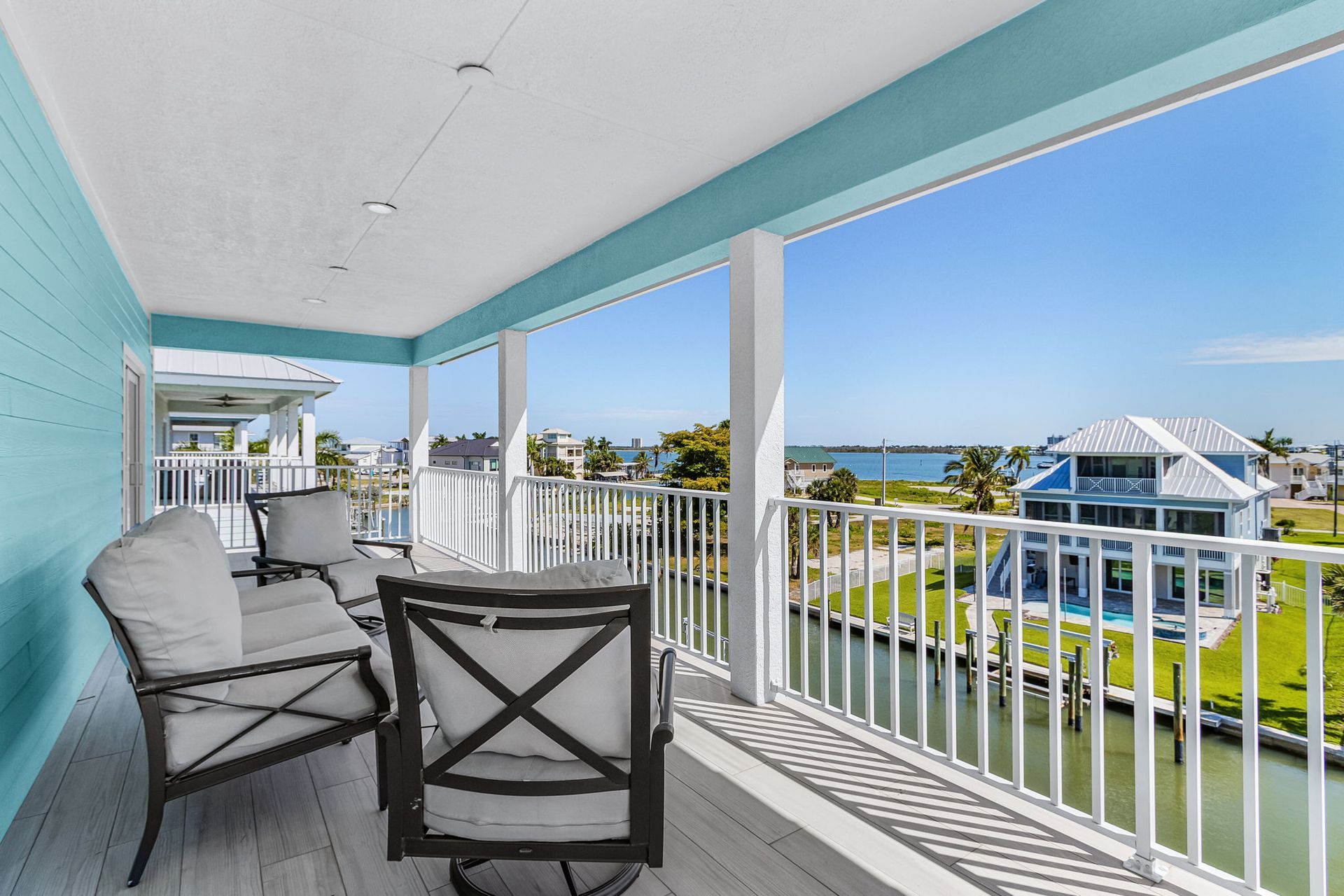 Covered balcony with white railings, blue walls, lounge chairs, and a waterfront view.