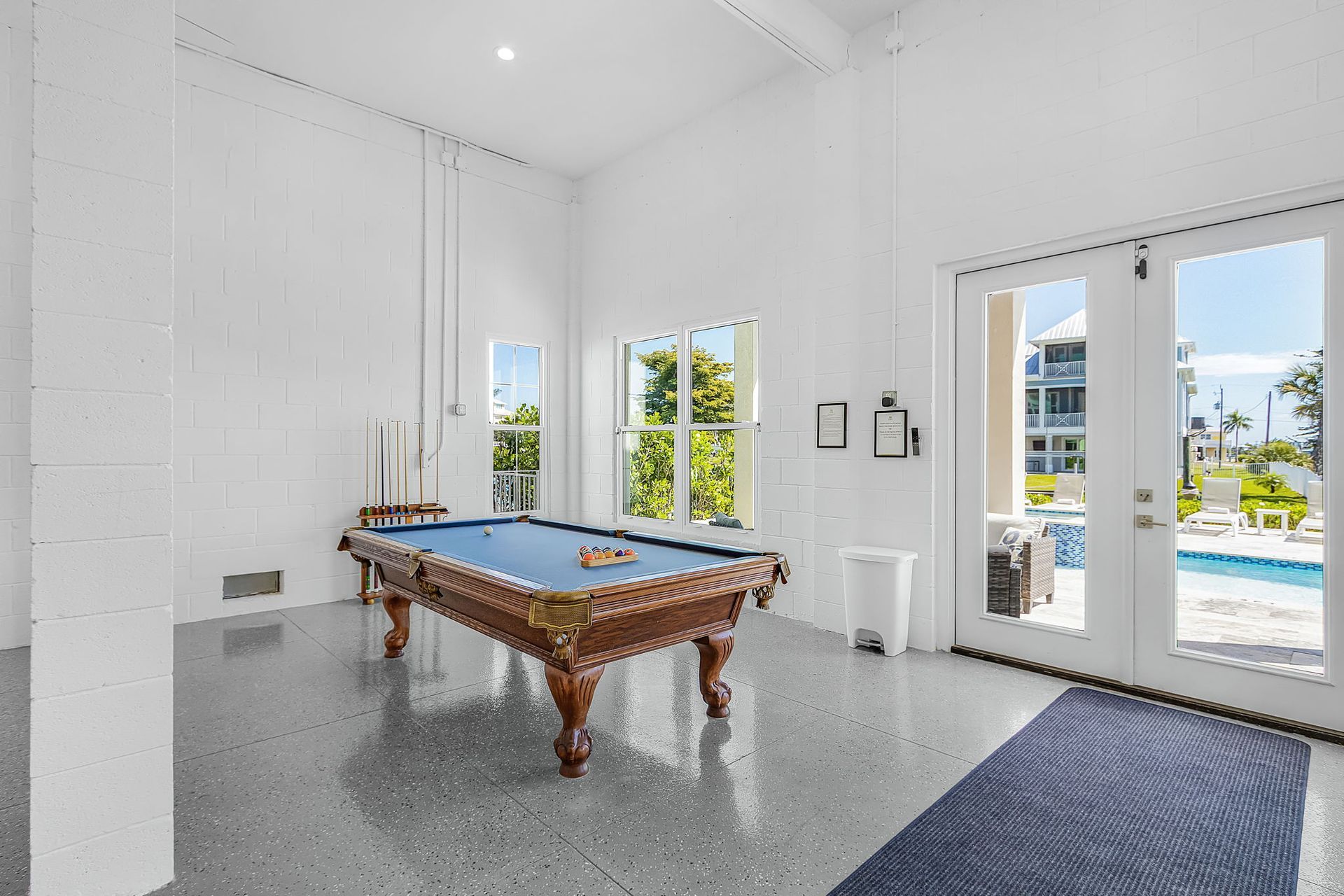 Bright game room with a pool table, white walls, large windows, and sliding doors to a patio and pool.