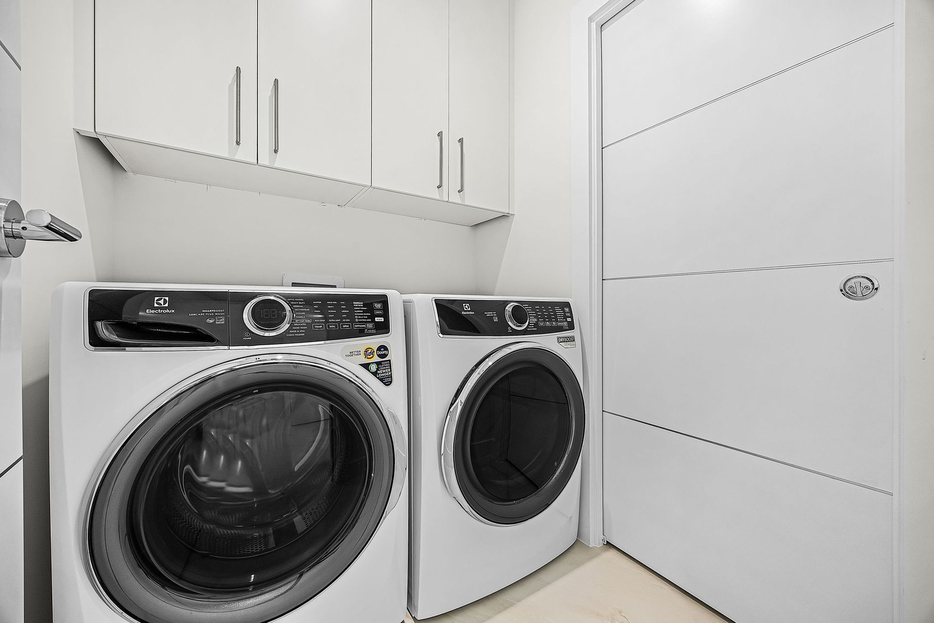 Laundry room with white washer and dryer, cabinets, shelf, and door.