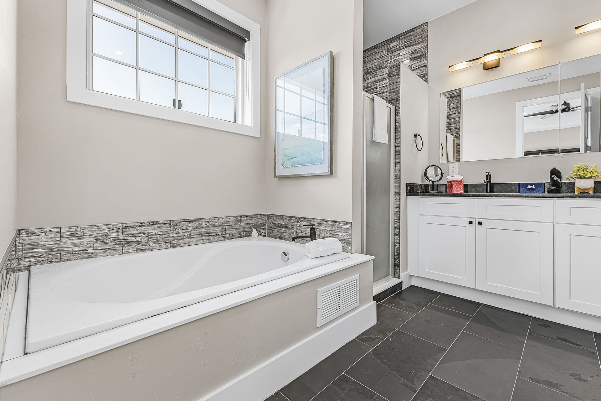 Modern bathroom with a white bathtub, dark tile floor, and vanity with large mirror and sink.