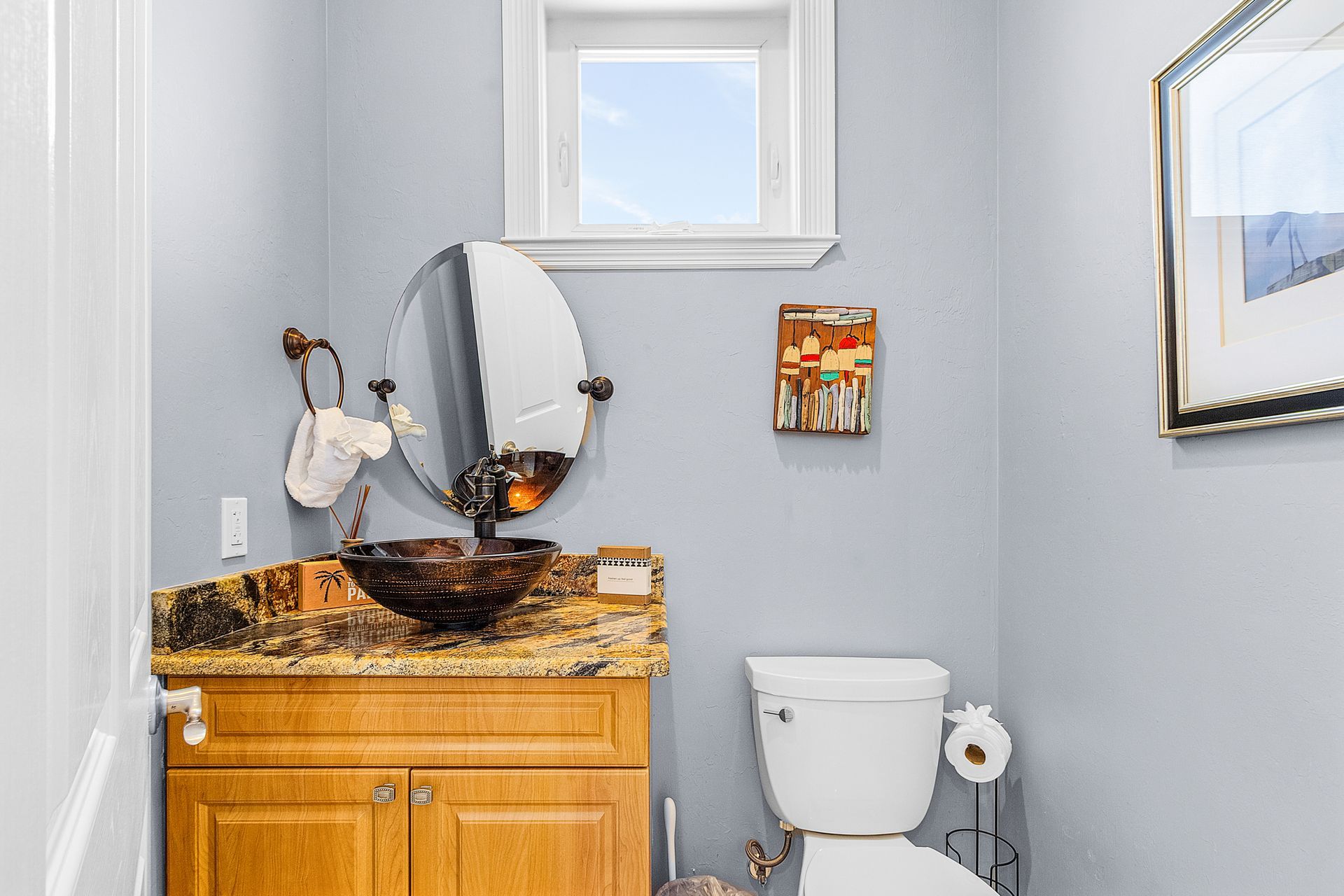 Small bathroom with a wooden vanity, round mirror, toilet, and window.