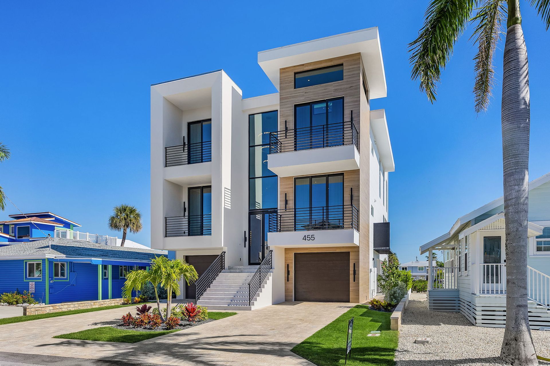Modern white house with balconies, garage, and palm tree on a sunny day.