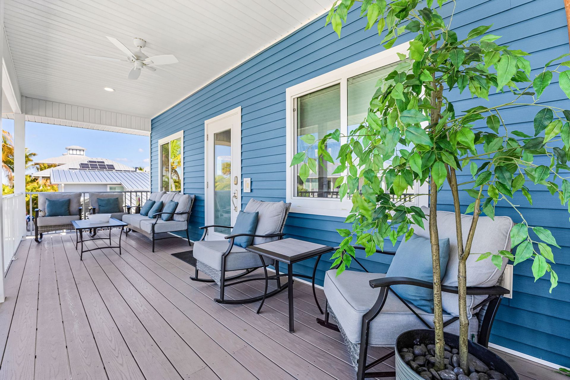 Blue porch with white wicker seating, gray decking, and potted plants along a house exterior