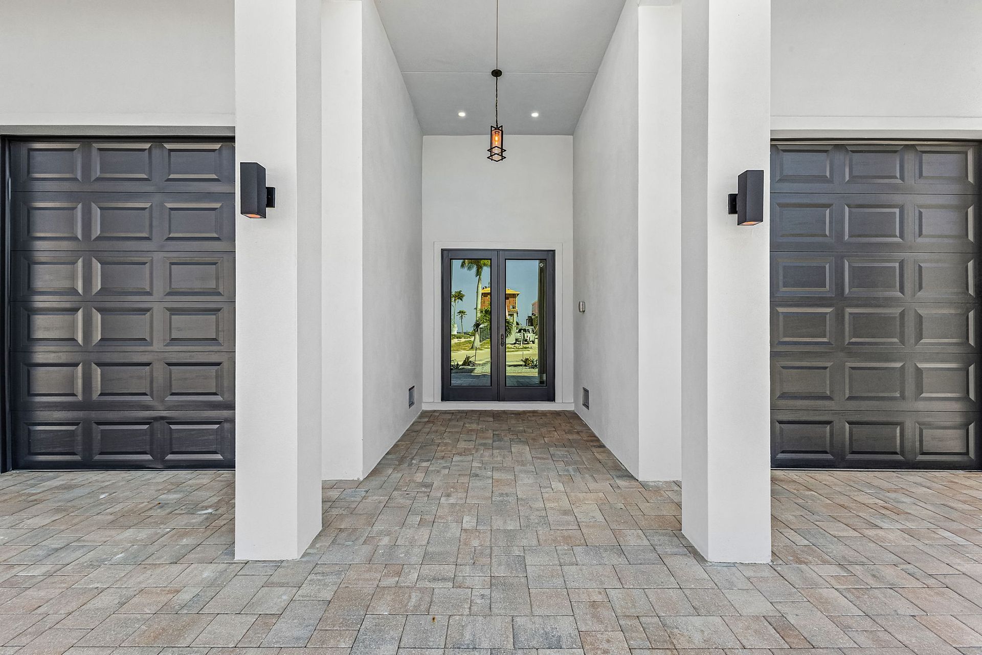 Modern building entrance with white columns, dark garage doors, and glass double doors at the end of a stone walkway